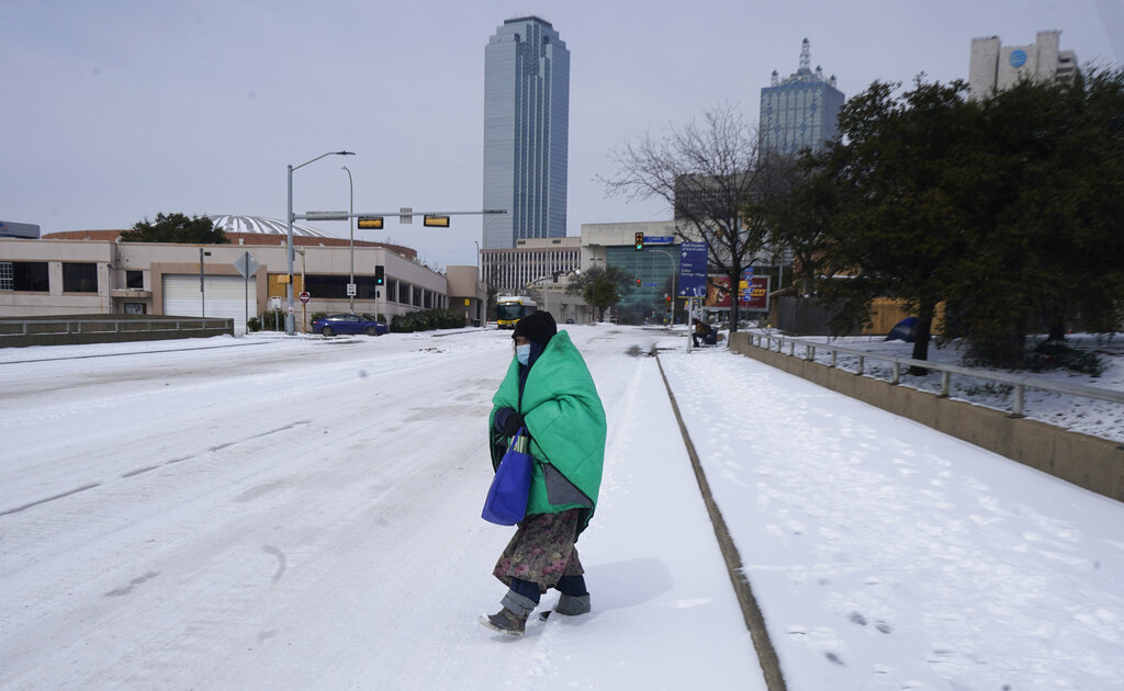 a woman wrapped in a blanket crosses the street