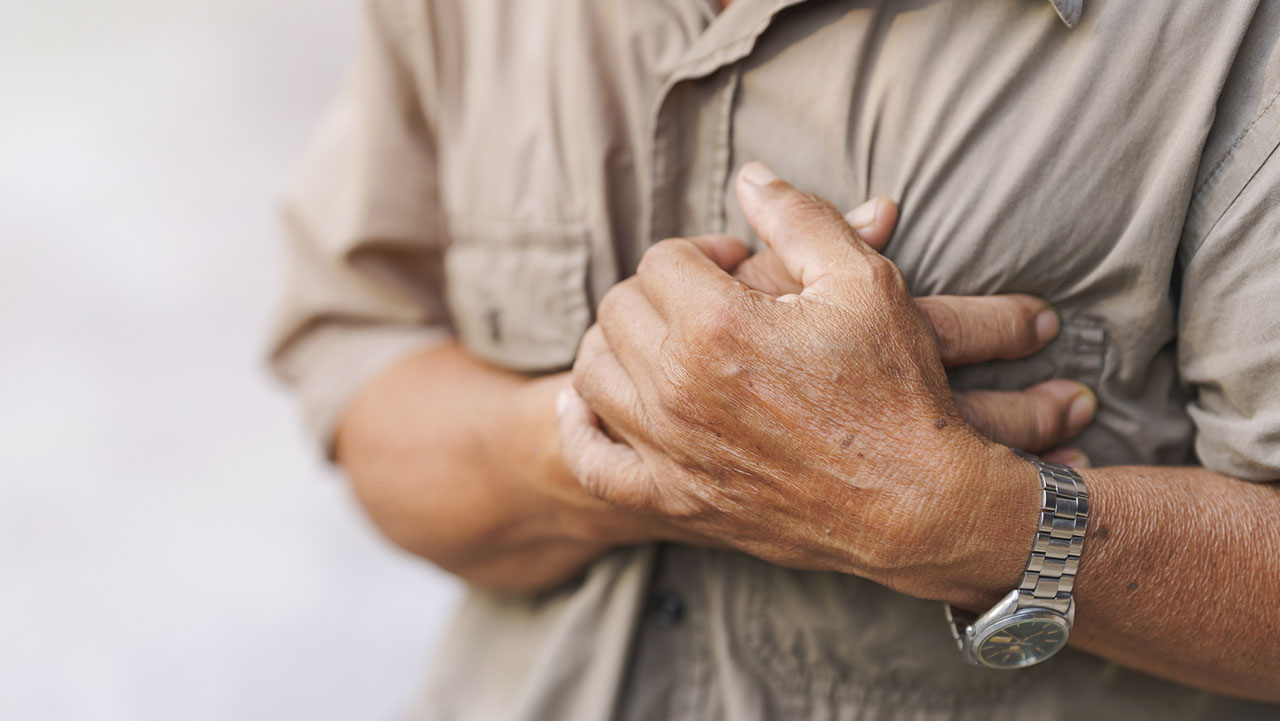 Close-up of an elderly man's hand held his chest in pain