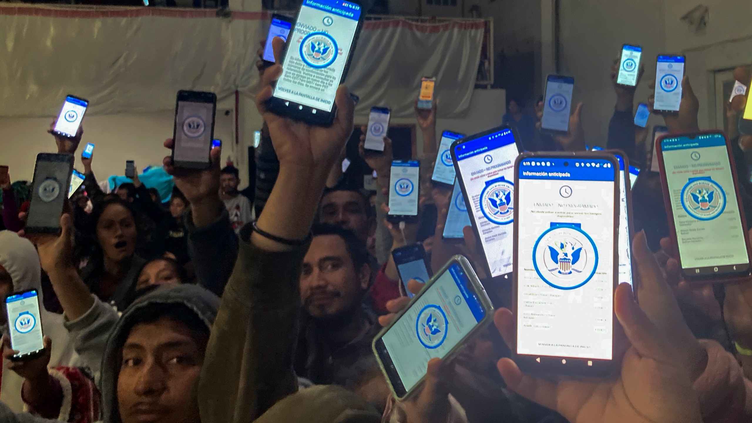 Migrants hold up their phones showing the CBP One app.