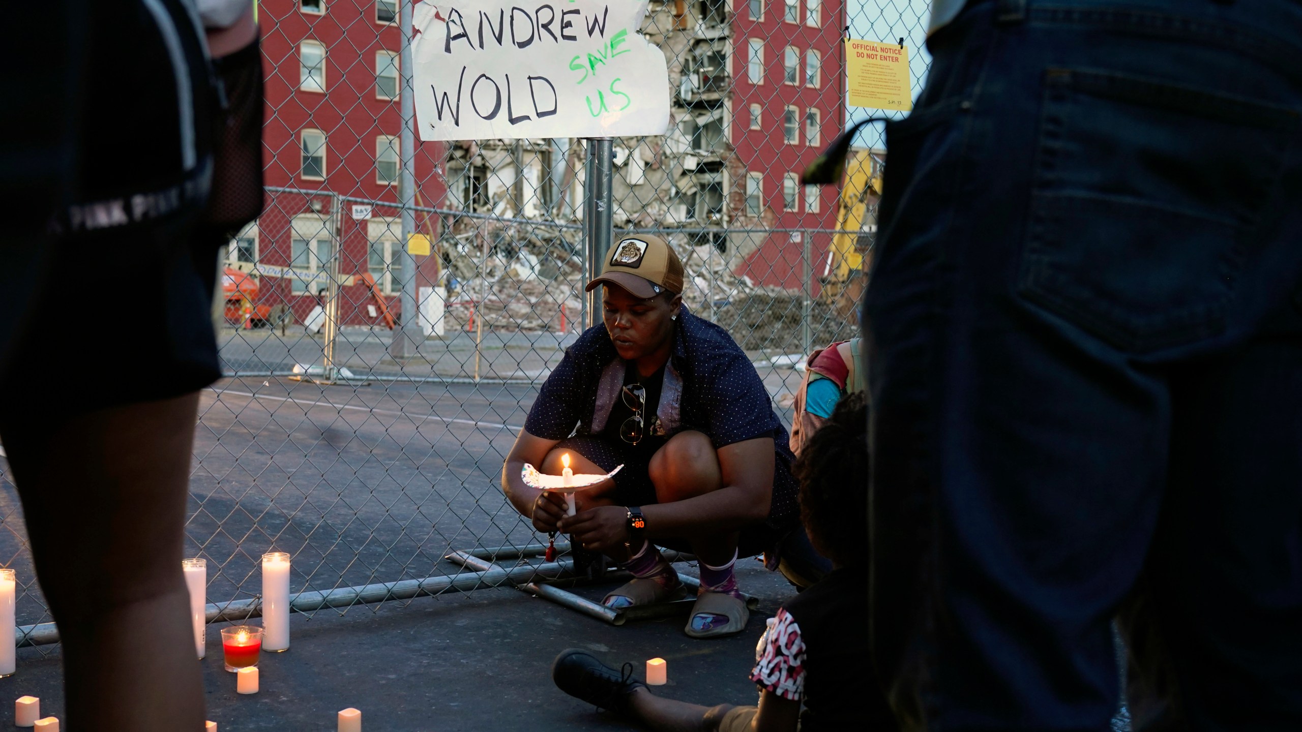 After asking a group of about 50 people gathered for a vigil to remain silent for five minutes in honor of the five people still unaccounted for, Raquel Sipp kneels with a candle at the scene of where an apartment building partially collapsed two days earlier, in Davenport, Iowa, Tuesday, May 30, 2023. Five residents of the six-story apartment building remained unaccounted for and authorities feared at least two of them might be stuck inside rubble that was too dangerous to search. (AP Photo/Erin Hooley)