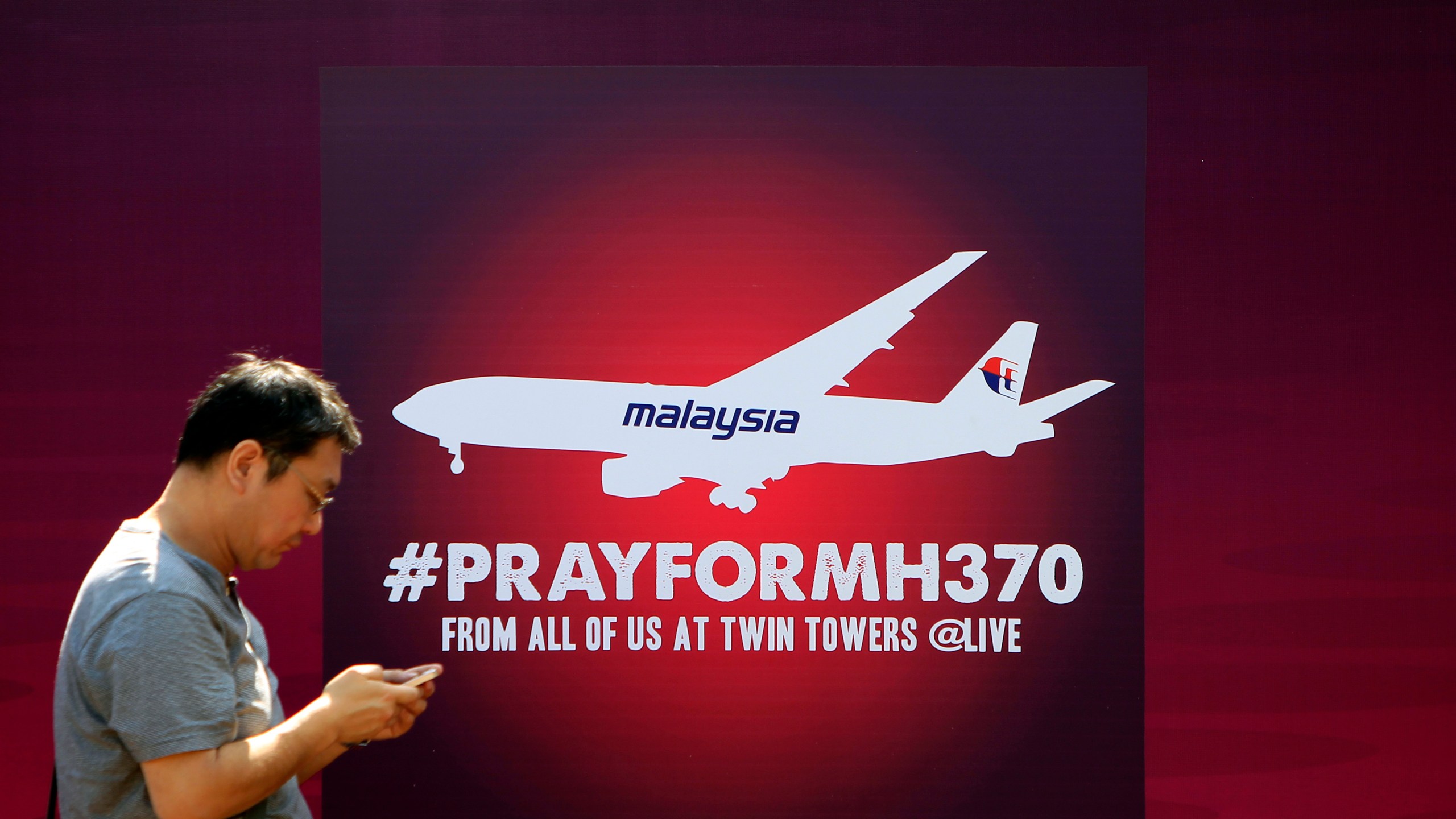 man walks past a board reading PRAY FOR MH370