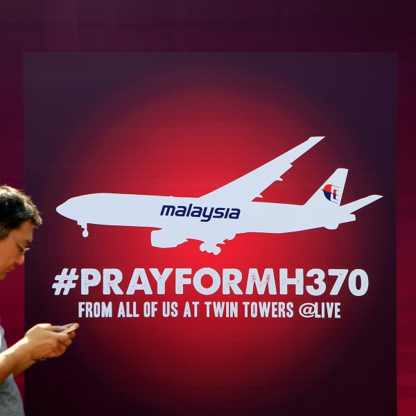 man walks past a board reading PRAY FOR MH370