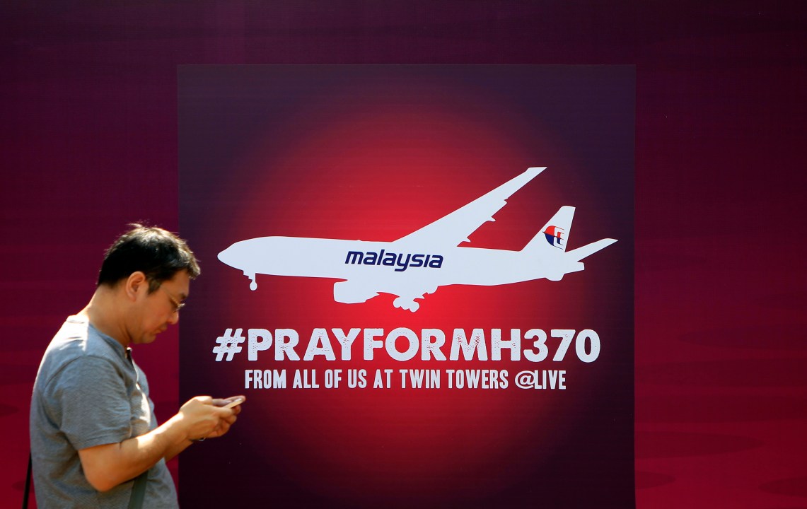 man walks past a board reading PRAY FOR MH370