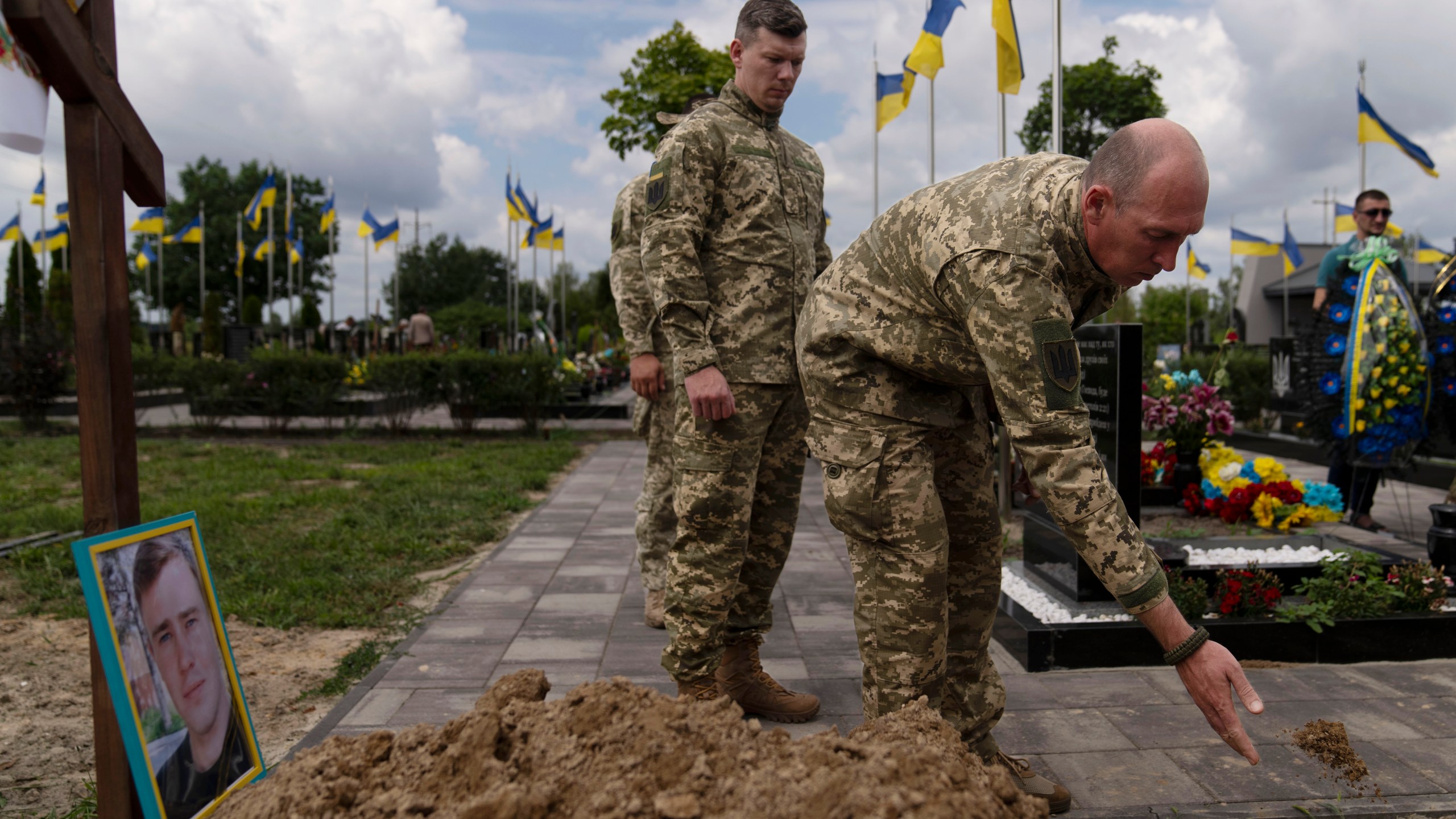 An Ukrainian soldier tosses dirt into the grave of Roman Shadlovskyi during a reburial service for him in Bucha, Ukraine, Tuesday, July 18, 2023. The Ukrainian Armed Forces veteran, who was initially buried in a mass grave as an unidentified victim after being killed last year by Russian troops, received a reburial Tuesday after a DNA test confirmed his identity. (AP Photo/Jae C. Hong)