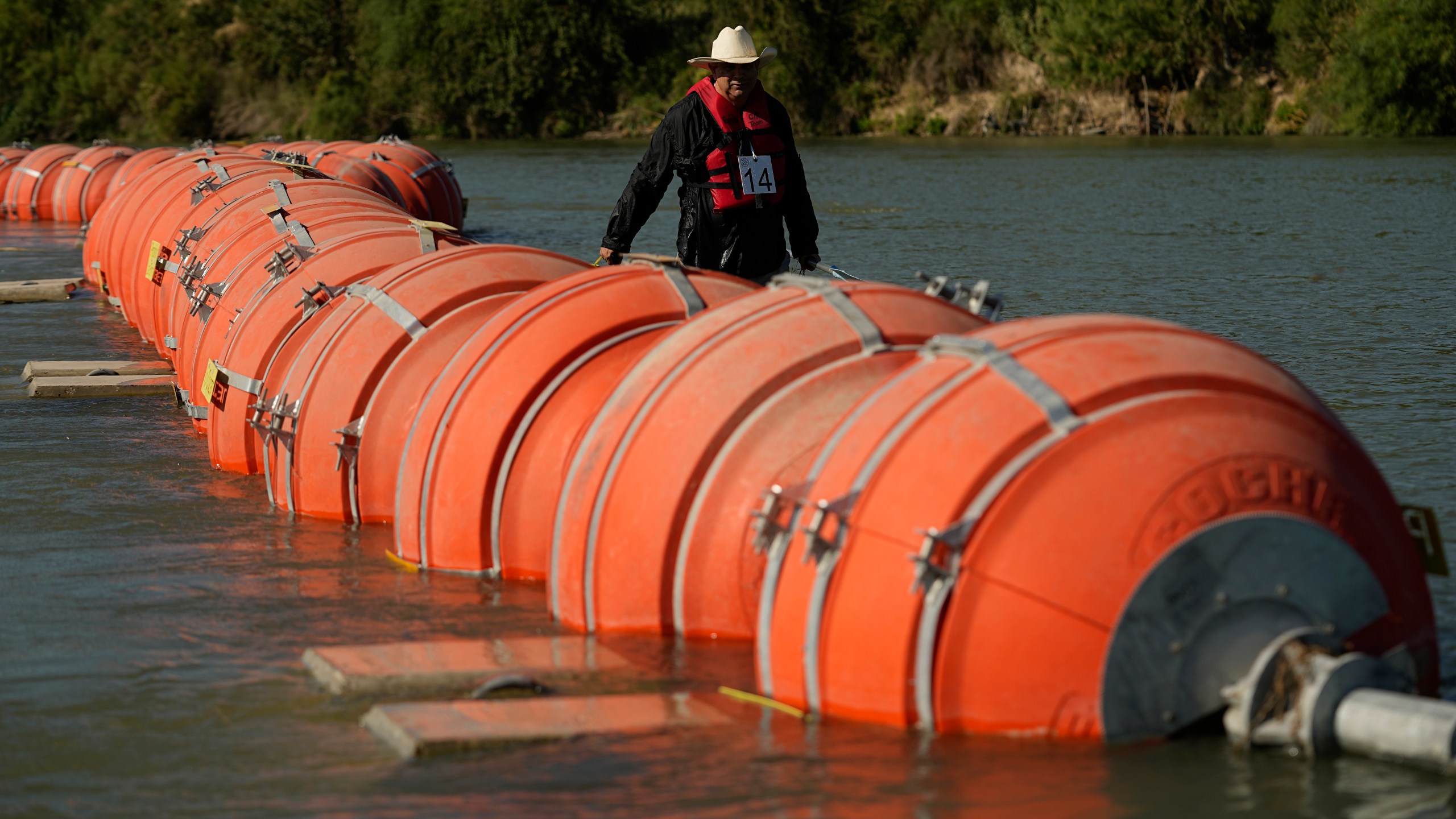 A kayaker walks past large buoys being used as a floating border barrier on the Rio Grande.
