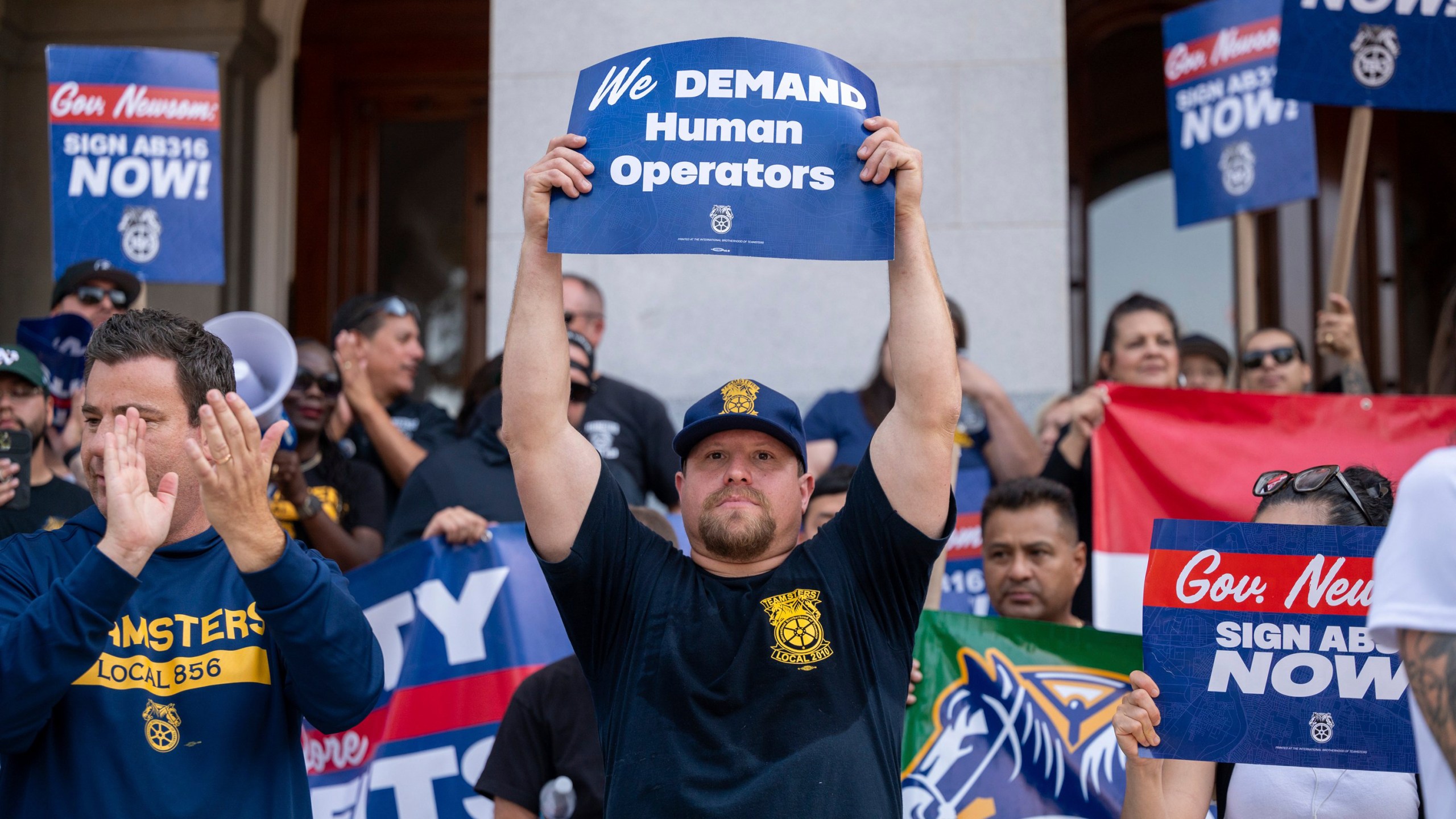 FILE- Teamsters union members hold signs urging Gov. Gavin Newsom to sign Assembly Bill 316, which would require in-person human supervision of self-driving vehicles weighing over 10,000 pounds, at the state Capitol in Sacramento, Calif., on Tuesday, Sept. 19, 2023. Gov. Gavin Newsom has vetoed a bill Friday, Sept. 22, 2023, that would have required human drivers to be onboard self-driving trucks, a measure that union leaders and truck drivers said would save hundreds of thousands of jobs. There are about 200,000 commercial truck drivers in California, according to Teamsters officials. (Paul Kitagaki Jr./The Sacramento Bee via AP, File)
