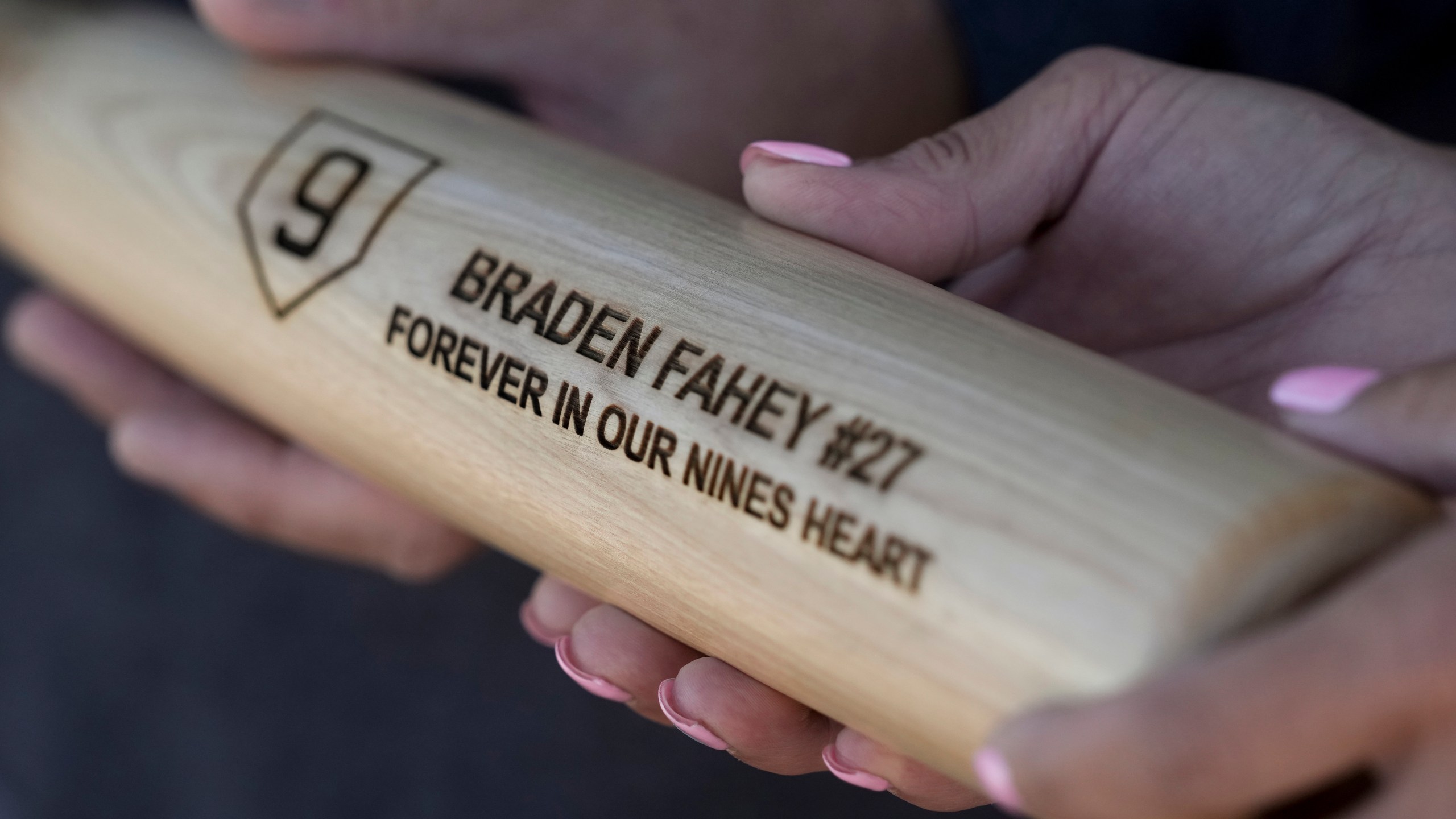 Padrig and Gina Fahey hold a bat dedicated to their son, Braden, by his baseball travel team Wednesday, Sept. 6, 2023, in California. Braden, 12, collapsed at a football practice last August and died of a malformed blood vessel in the brain. (AP Photo/Godofredo A. Vásquez)