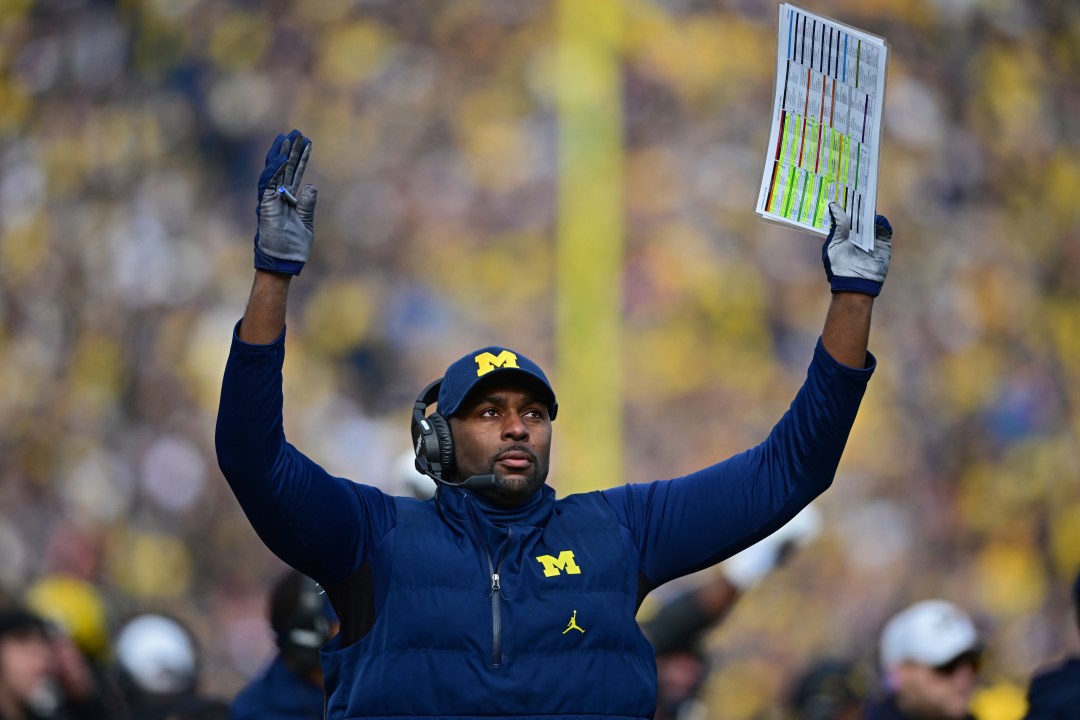  Sherrone Moore coaching from the sidelines with arms raised