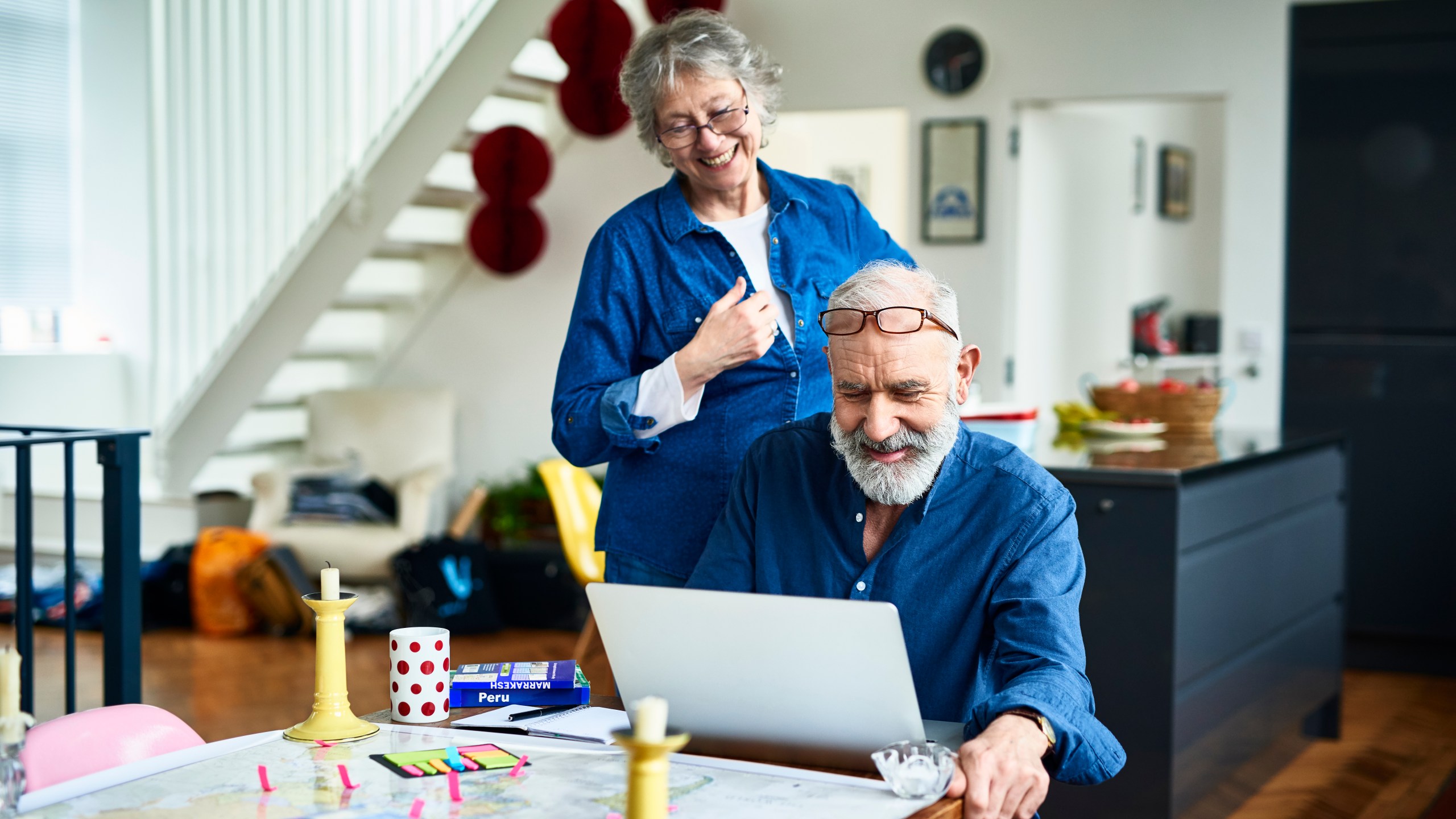 Senior woman smiling and looking over husband's shoulder as he uses a computer