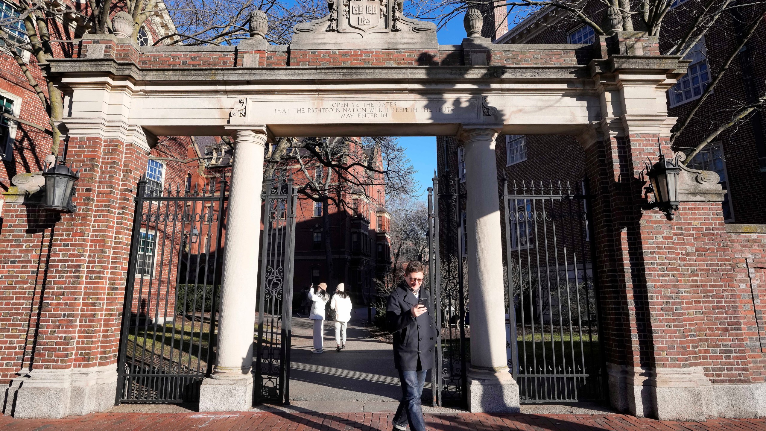 A passer-by walks through a gate to the Harvard University campus, Tuesday, Jan. 2, 2024, in Cambridge, Mass. Harvard University President Claudine Gay resigned Tuesday amid plagiarism accusations and criticism over testimony at a congressional hearing where she was unable to say unequivocally that calls on campus for the genocide of Jews would violate the school's conduct policy. (AP Photo/Steven Senne)