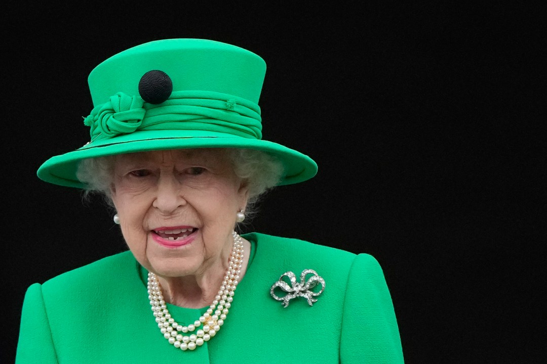 Queen Elizabeth II stands on the balcony in a green suit and hat