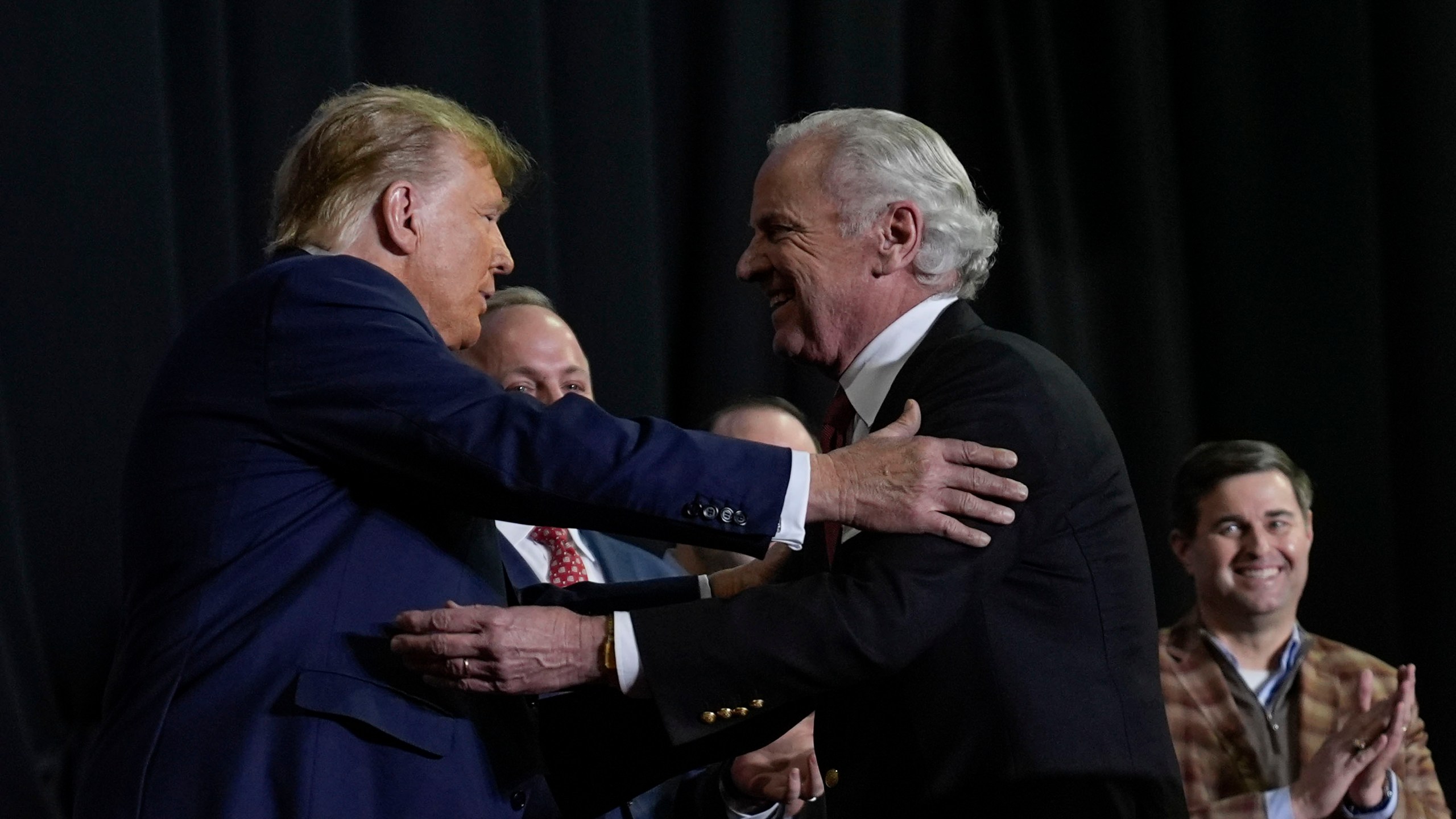 Republican presidential candidate former President Donald Trump, left, and South Carolina Gov Henry McMaster, right, embrace on stage during a campaign event in Manchester, N.H., Saturday, Jan. 20, 2024. Also on stage is South Carolina House Speaker Murrell Smith, far right. (AP Photo/Matt Rourke)