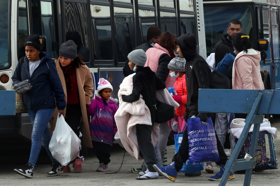 Dozens of migrants, carrying their belongings in bags, board CTA warming buses after being dropped off in Chicago.