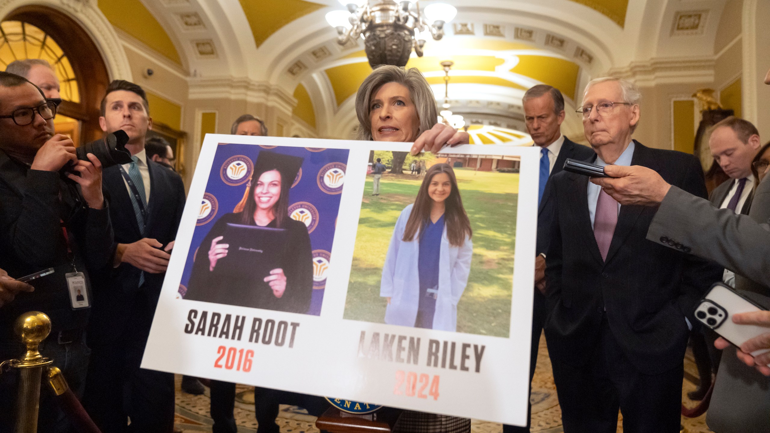 Sen. Joni Ernst, R-Iowa, holds a poster with photos of murder victims Sarah Root and Laken Riley