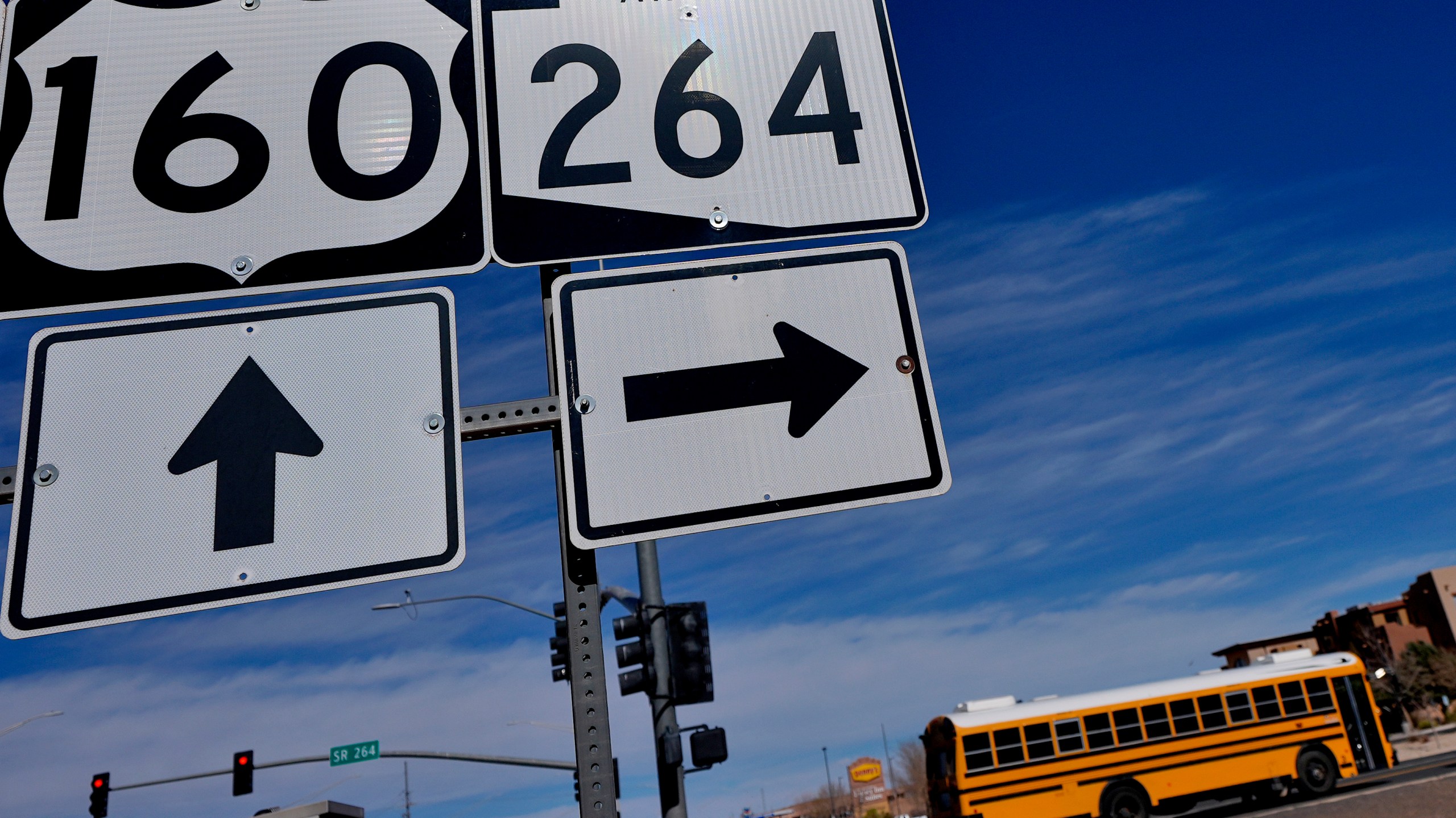 A school bus crosses over U.S. 160 from the Navajo Nation, left, onto the Hopi reservation, right, Monday, March 4, 2024, in Tuba City, Ariz. U.S. Highway 160 is the de facto border between the Navajo and Hopi Indian reservations and two time zones. Mind-bending time calculations is what people in the largest Native American reservation in the U.S. have to endure every March through November. The Navajo Nation, which stretches into Utah and New Mexico, will reset clocks for one hour later despite the rest of Arizona remaining on standard time. (AP Photo/Matt York)