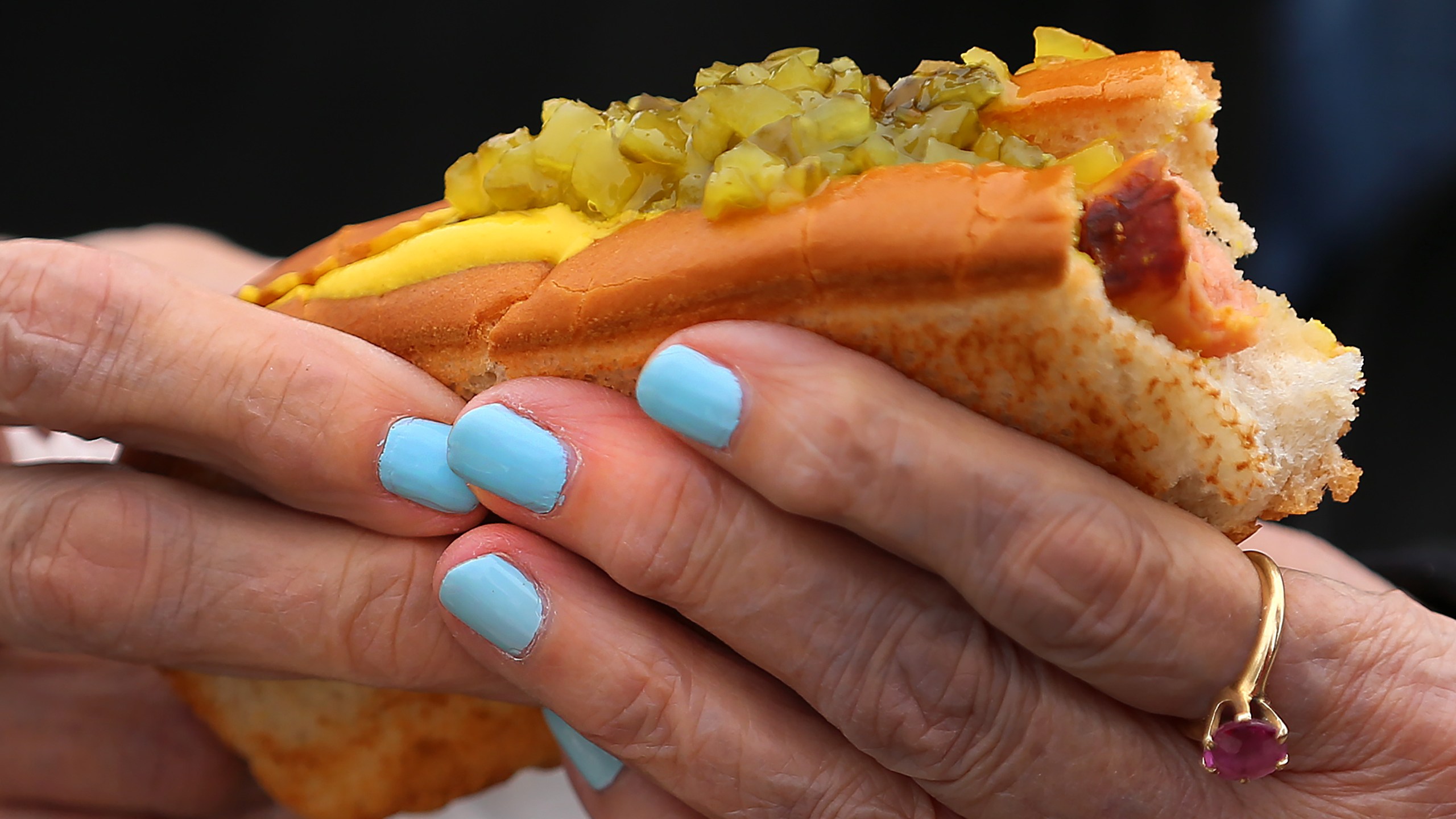 A woman eats a hot dog with relish and mustard