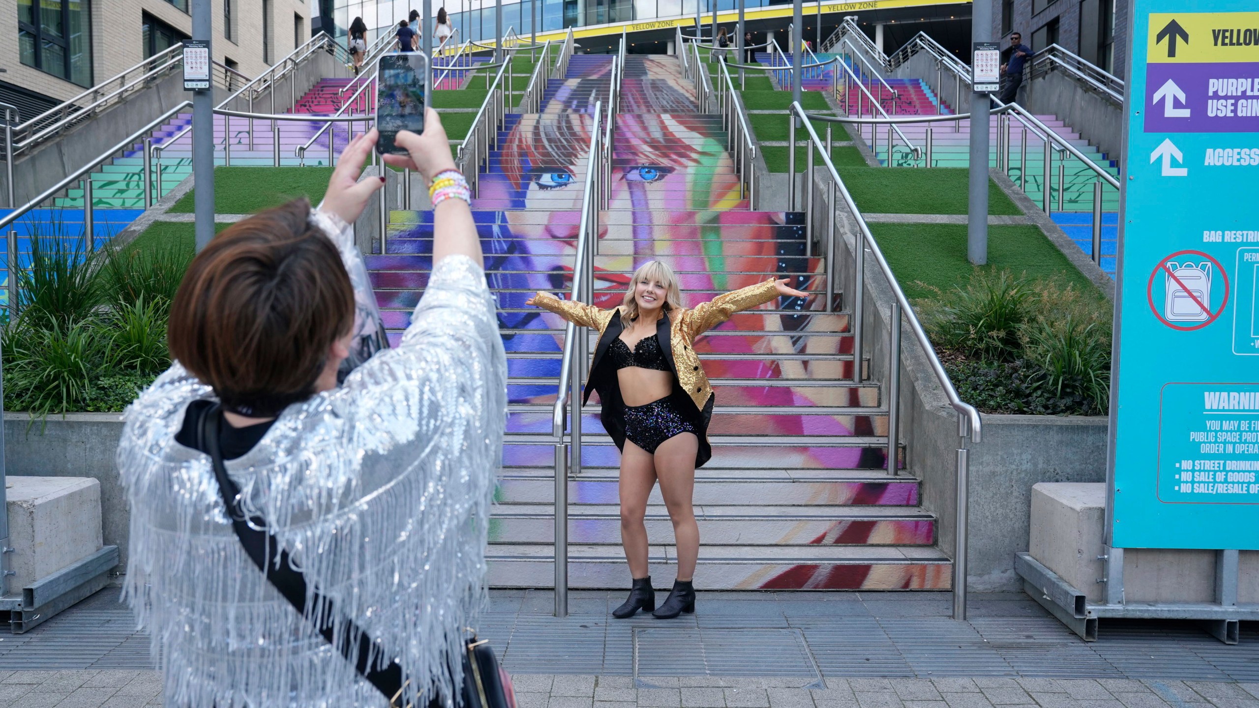 A fan poses for a photo by a staircase with the image of Taylor Swift, outside Wembley Stadium ahead of her first London concert, during the Eras Tour, in London, Friday June 21, 2024. (Lucy North/PA via AP)