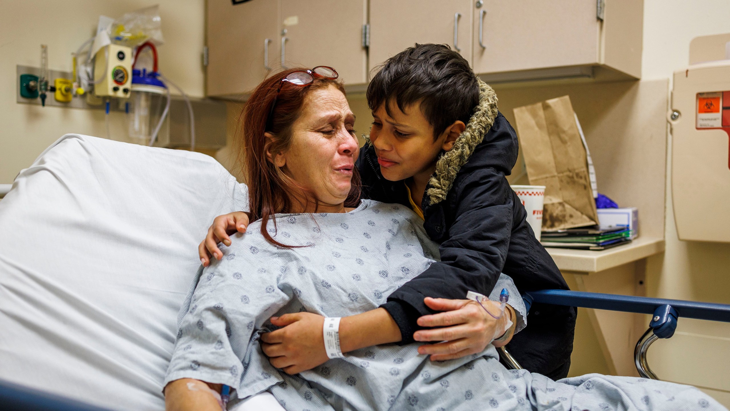 A young boy hugs his mother as she lay in a hospital bed