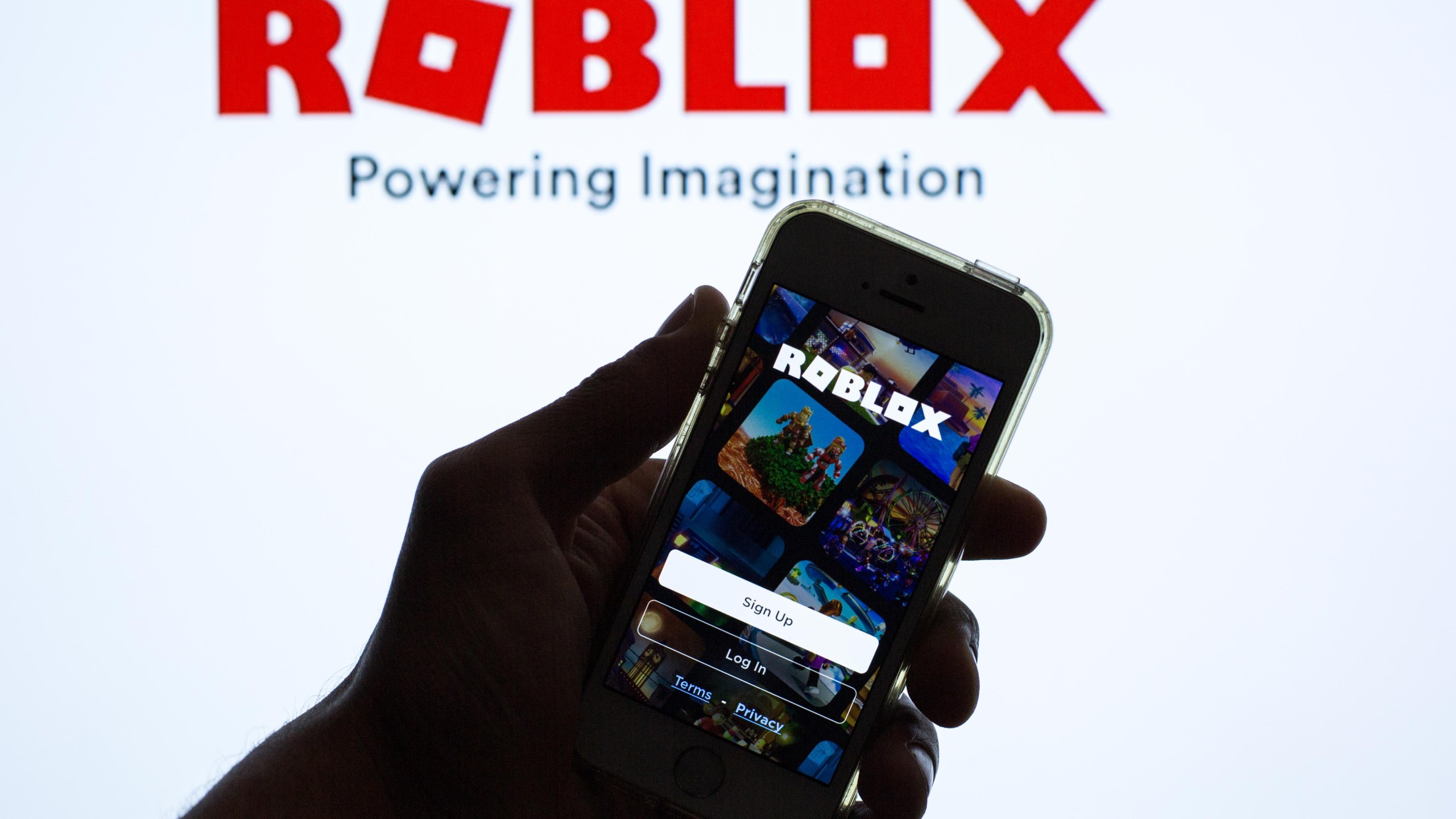 In this photo illustration, the Roblox app seen displayed on a smartphone screen and a Roblox logo in the background.