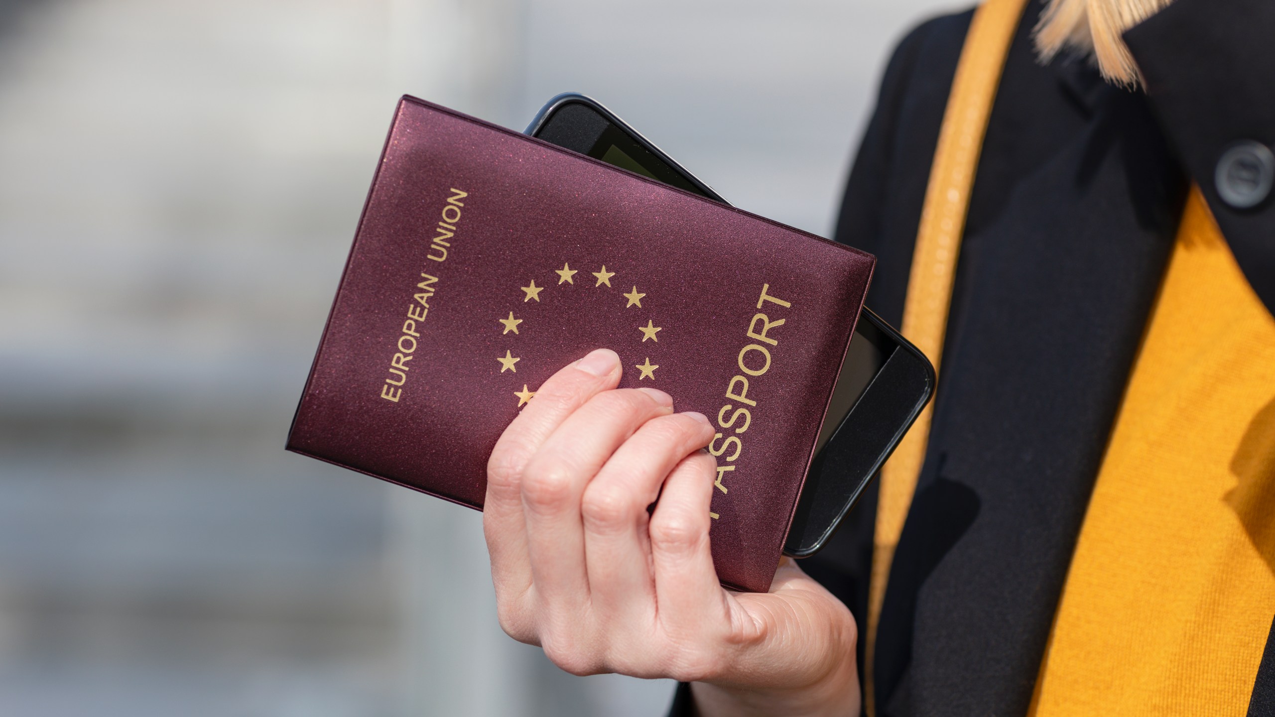 Close up of woman hand holding European Union Passport and mobile phone.