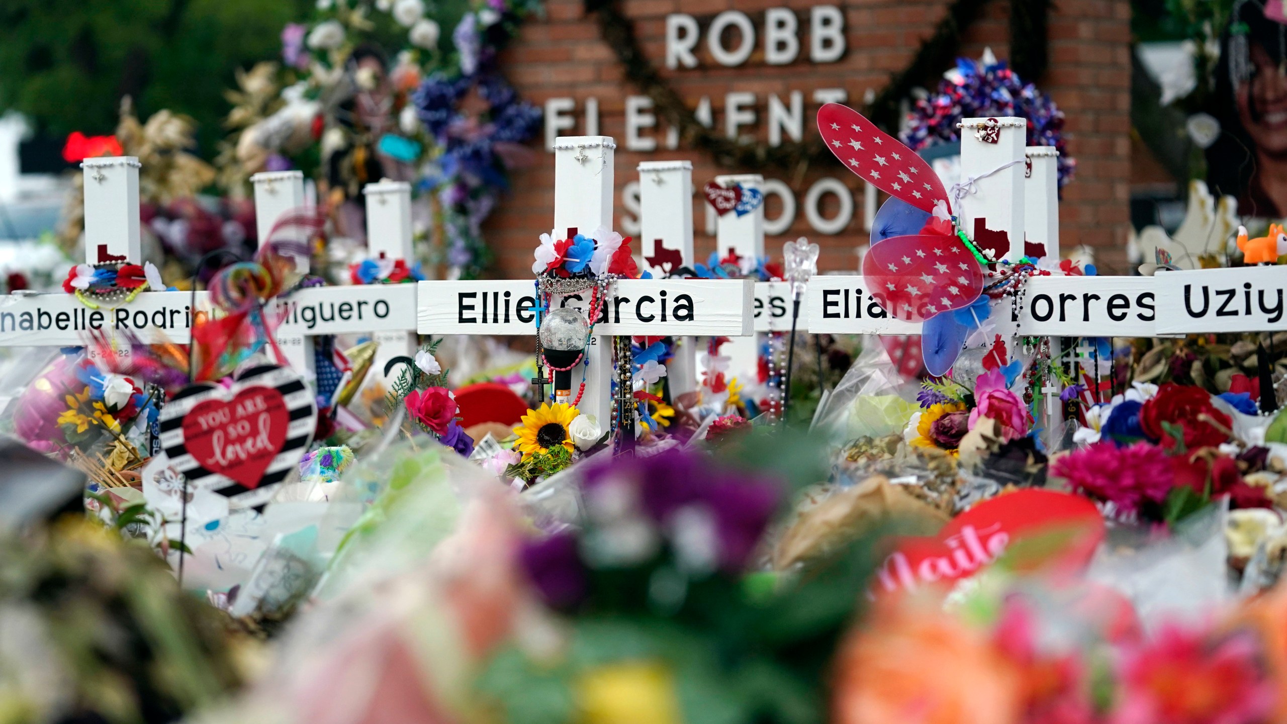 Crosses are surrounded by flowers and other items at a memorial