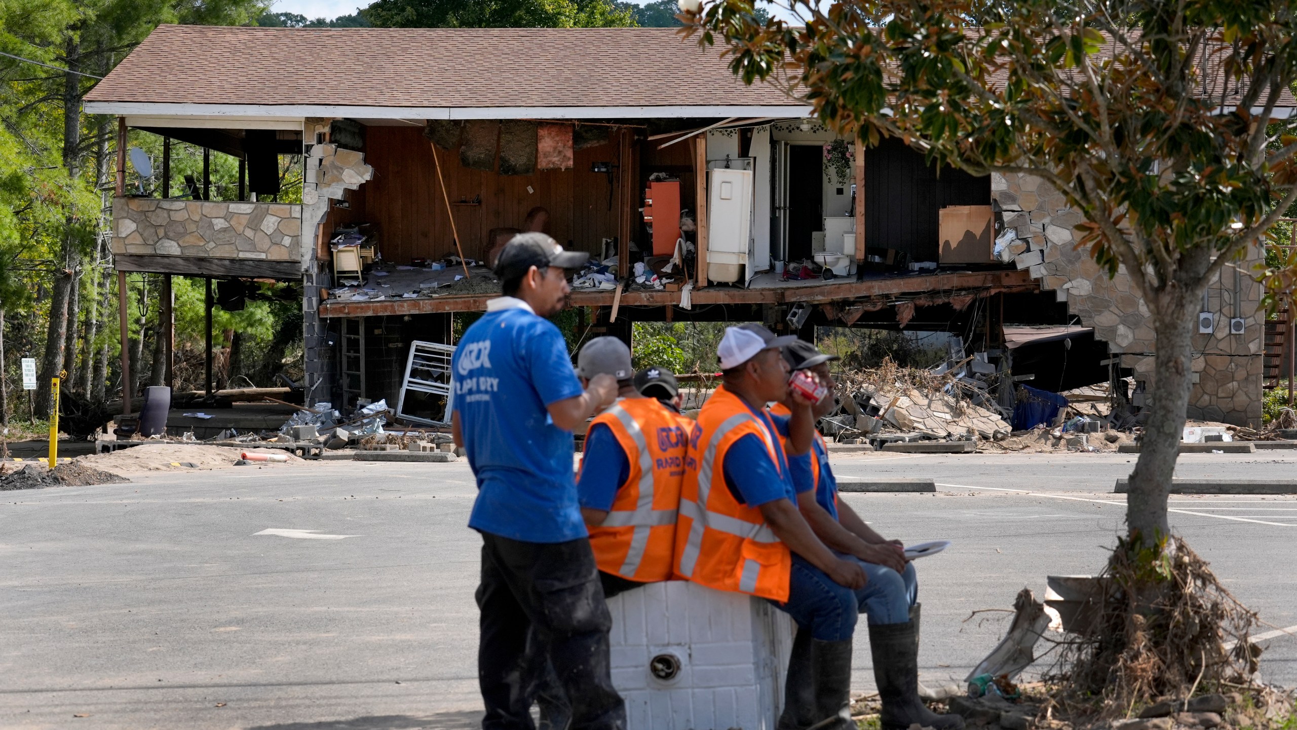 Workers helping with clean up efforts stop for lunch under the shade of a tree as a building destroyed by Hurricane Helene is seen in the background Saturday, Oct. 5, 2024, in Newport, Tenn. (AP Photo/Jeff Roberson)