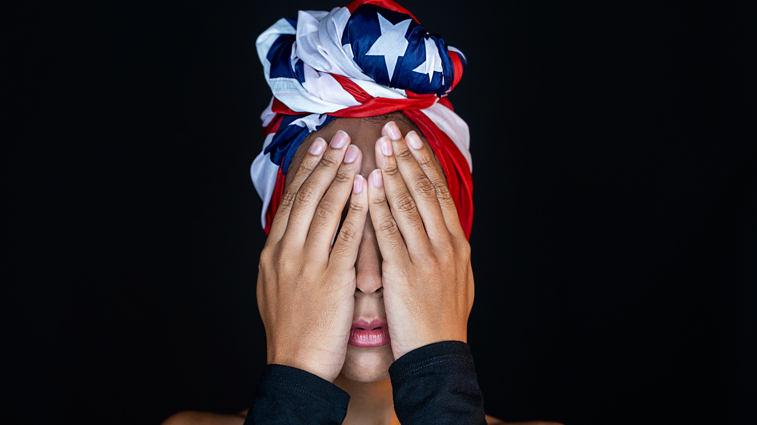 Horizontal close up view of mixed race woman isolated on black background wearing an American Flag. protests concept.