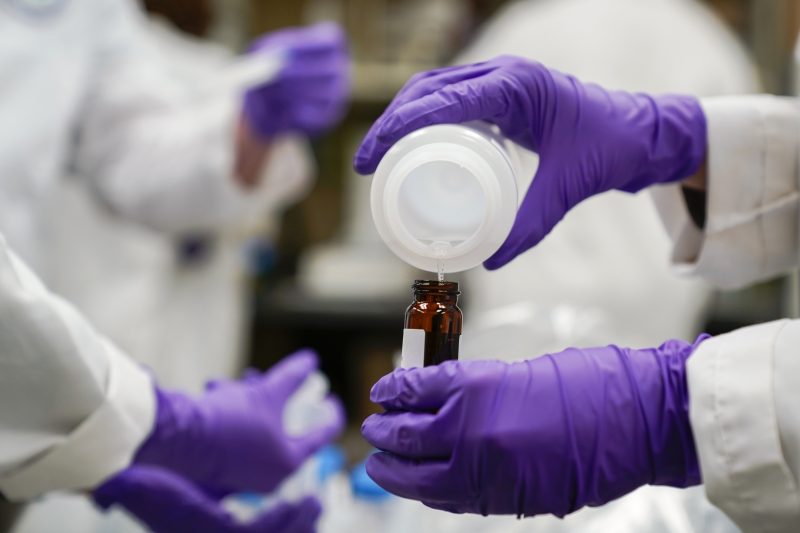 researcher pours liquid into a glass container in a lab
