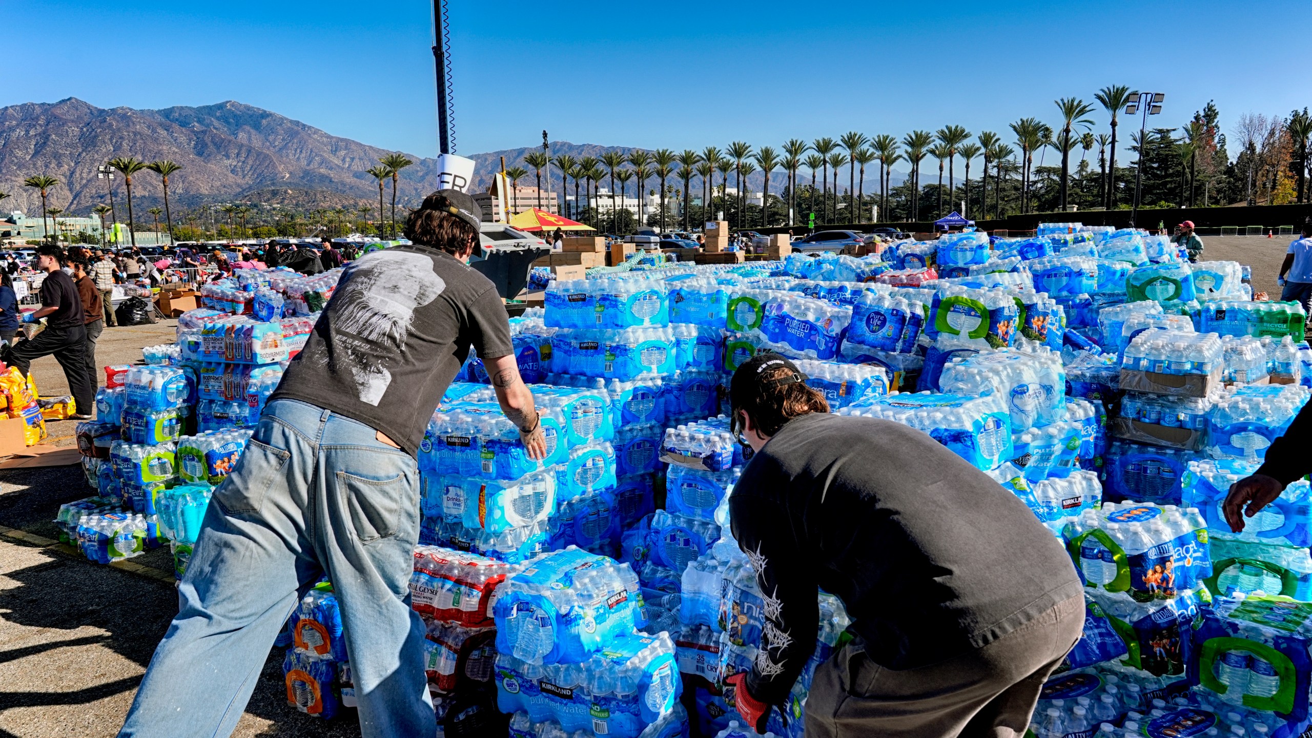 Volunteers stack donated water for people impacted by the Altadena Fire at a donation center at Santa Anita Park in Arcadia, Calif., on Wednesday, Jan. 15, 2025. (AP Photo/Richard Vogel)