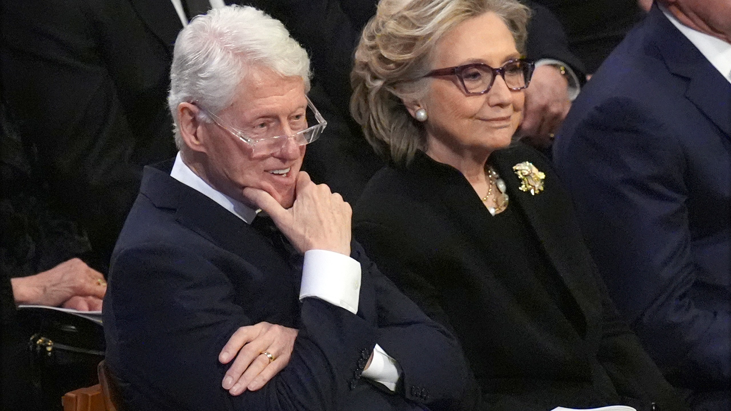 Bill and Hillary Clinton sitting during a funeral