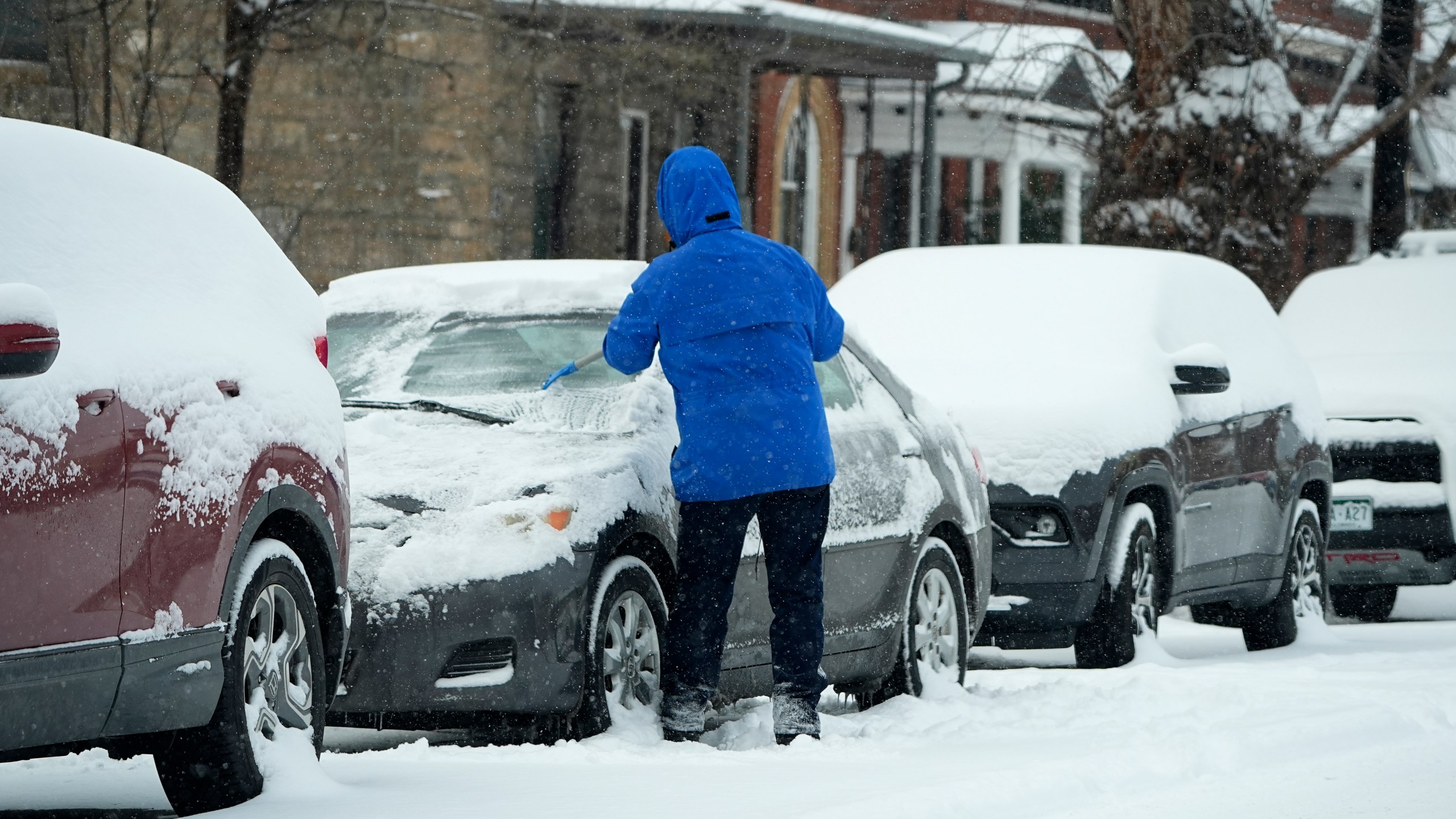 A motorist clears ice and snow from the windshield of a vehicle as a winter storm sweeps over the intermountain West, plunging temperatures into the single digits and bringing along a light snow in its wake Saturday, Jan. 18, 2025, in Denver. (AP Photo/David Zalubowski)