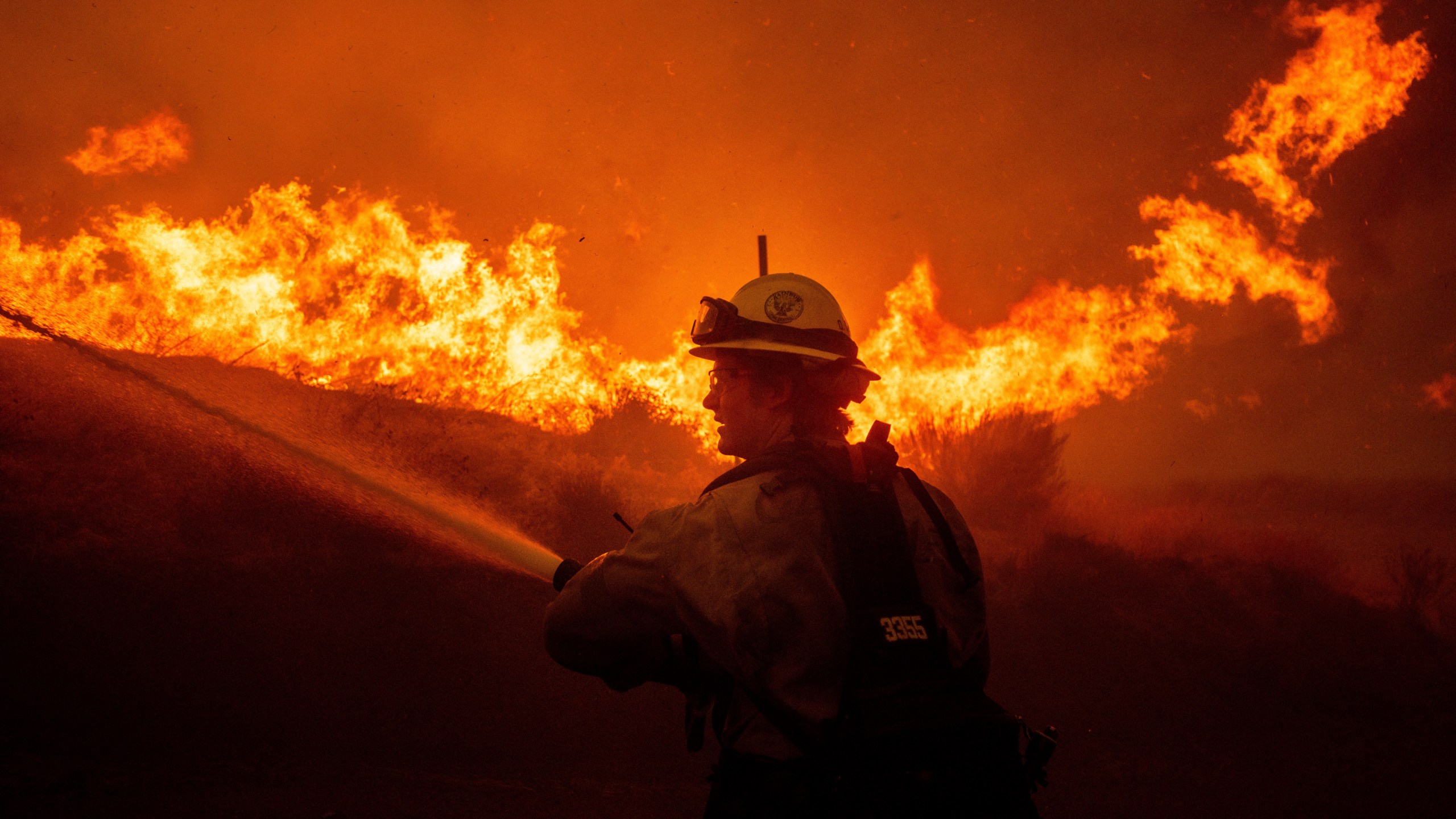 A firefighters spray water as he monitor flames caused by the Hughes Fire along a roadside in Castaic, Calif., Wednesday, Jan. 22, 2025. (AP Photo/Ethan Swope)