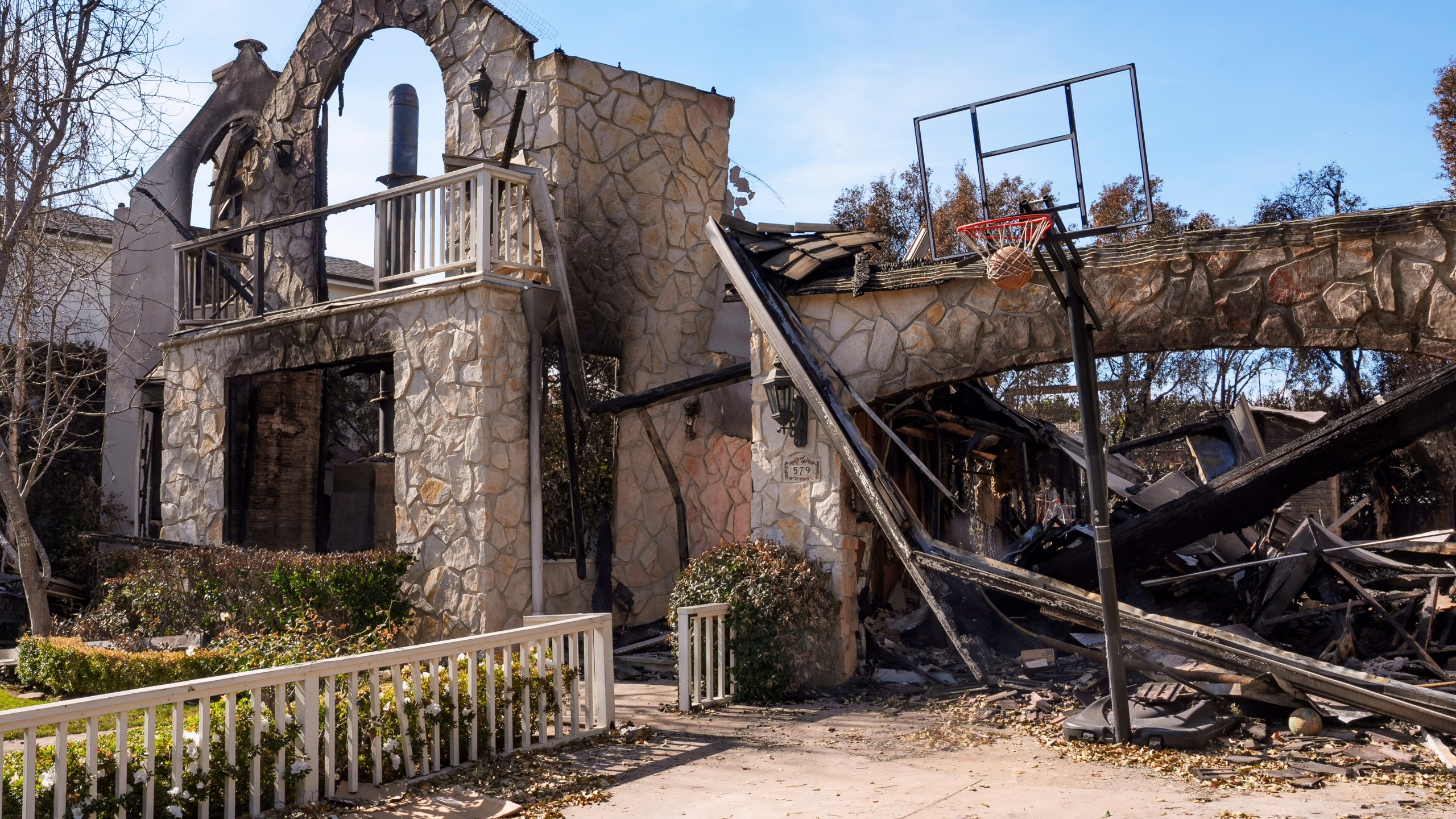 A basketball is stuck in the net outside of a residence destroyed by the Palisades Fire in the Pacific Palisades neighborhood of Los Angeles, Friday, Jan. 24, 2025. (AP Photo/Damian Dovarganes)