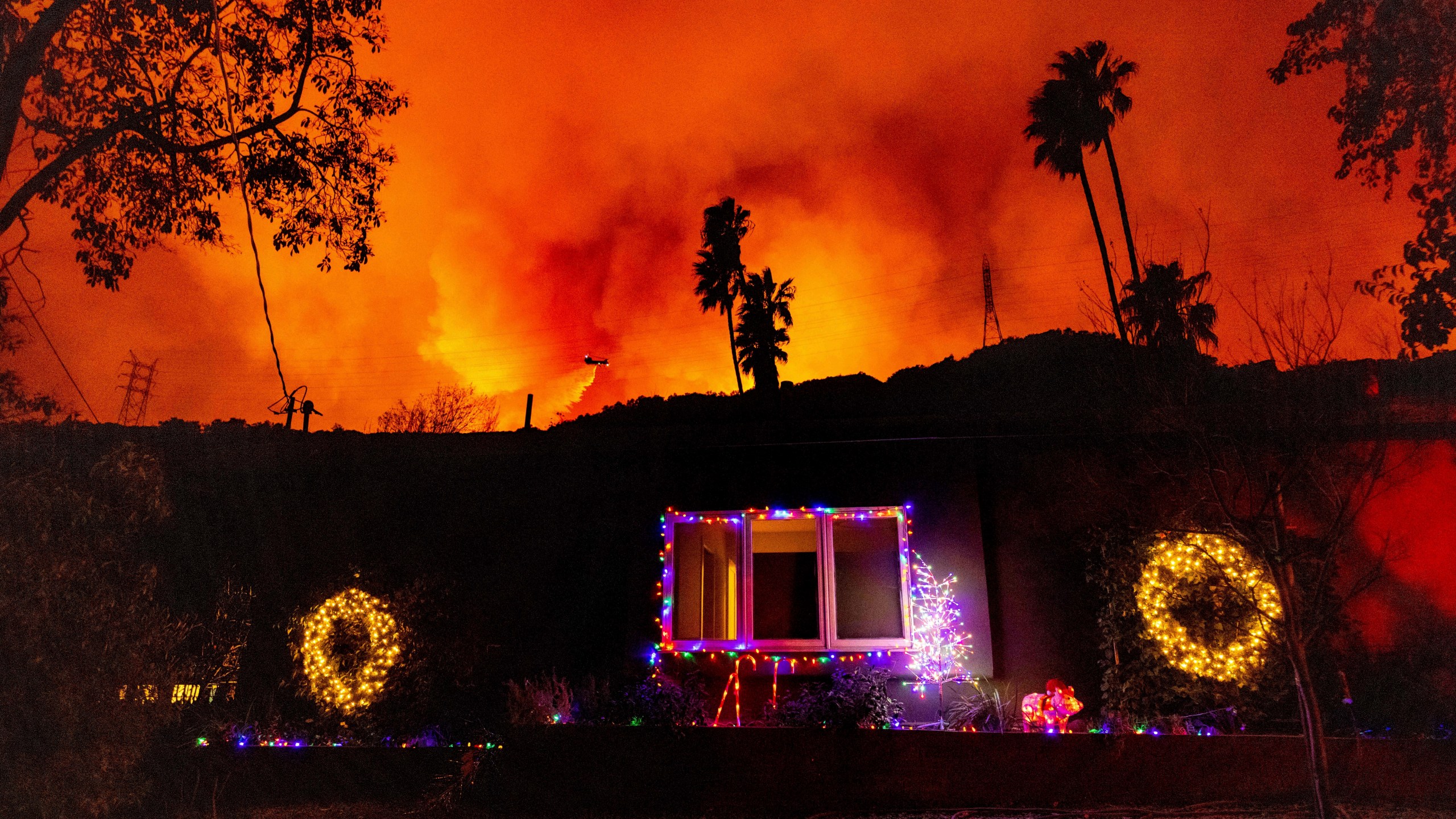 A helicopter drops water as fire rages behind a home decorated for Christmas.