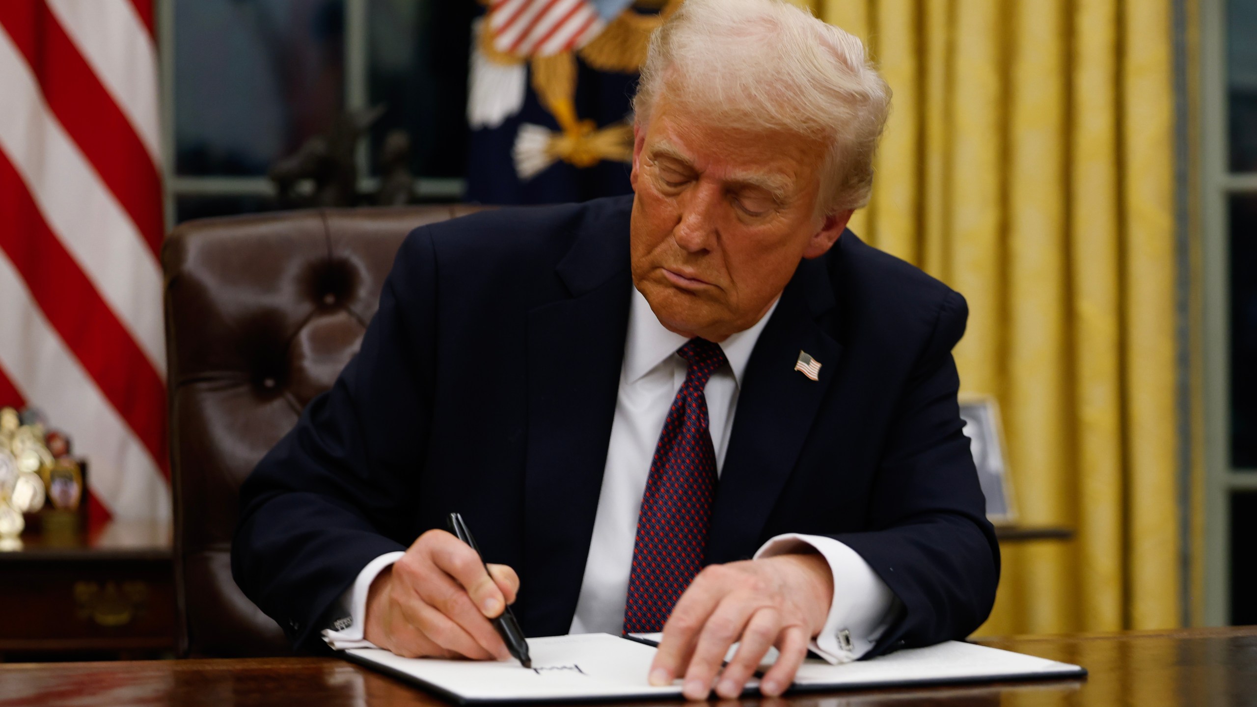 President Trump signing a document at his desk in the Oval Office