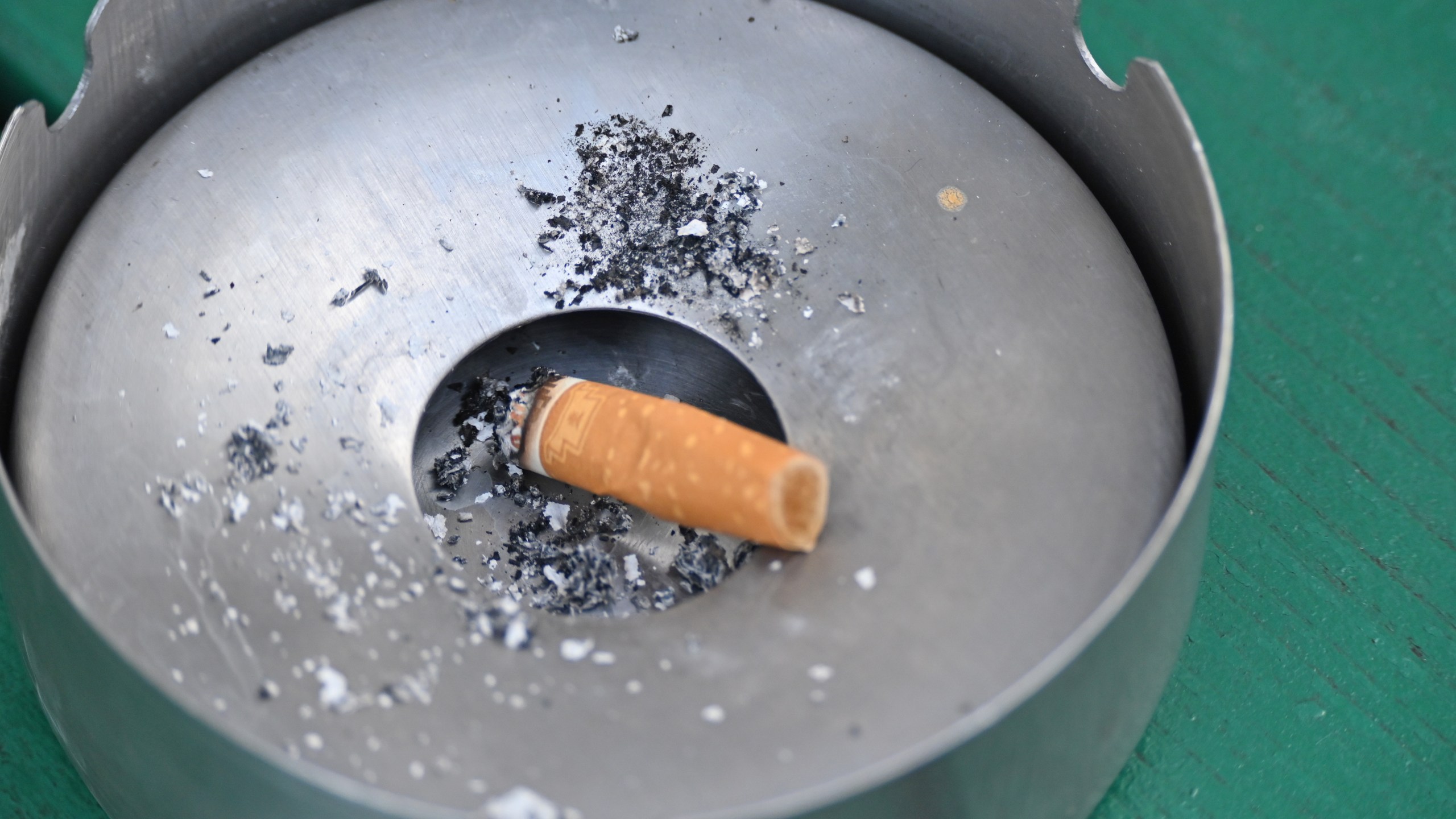 A burnt cigarette lies in an ashtray outside.
