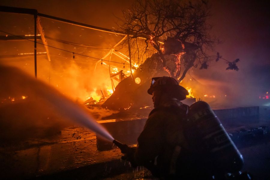 A firefighter fights the flames from the Palisades fire burning the Theatre Palisades during a powerful windstorm.
