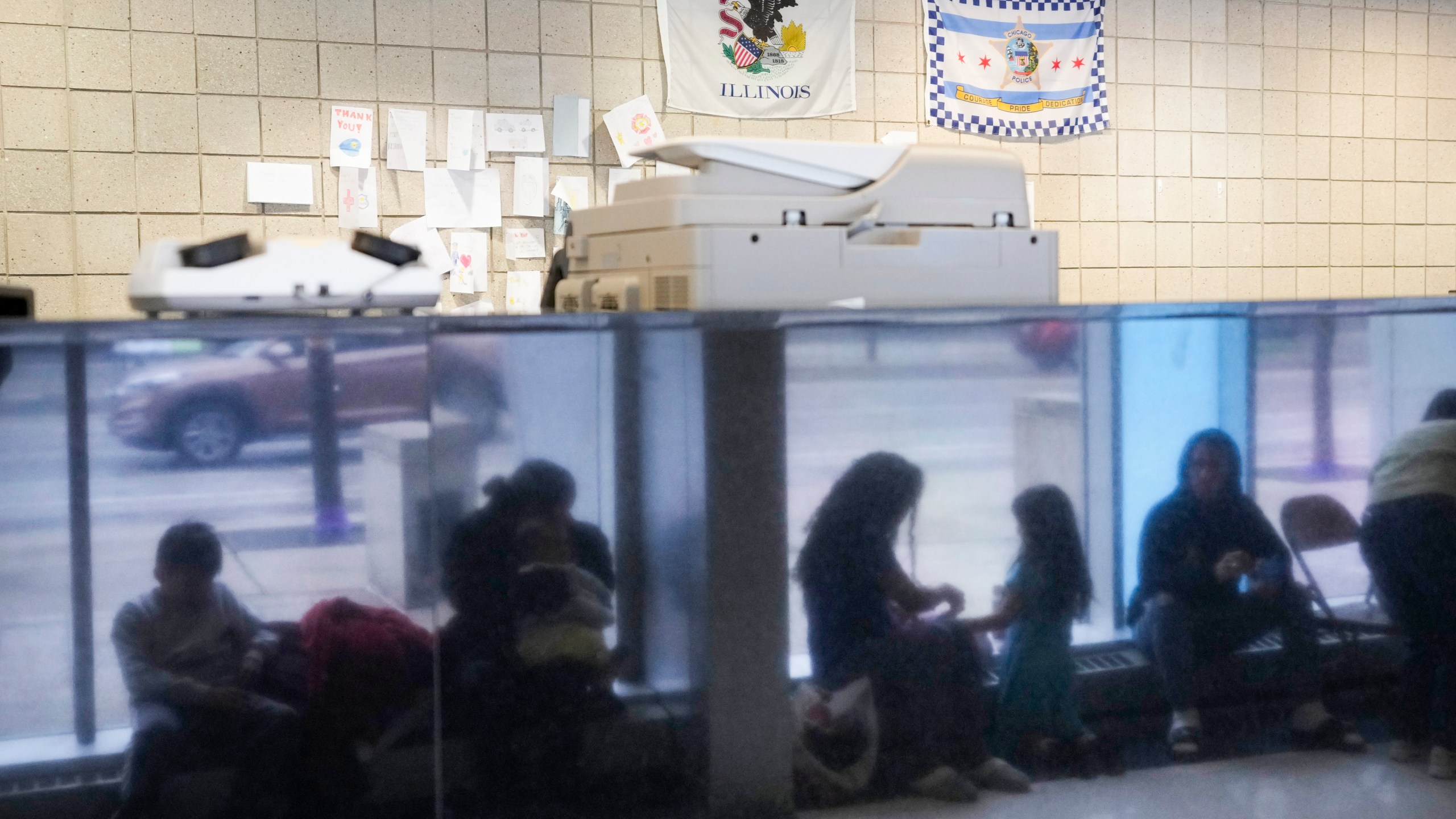 FILE - Immigrants from Venezuela are reflected in a marble wall while taking shelter at the Chicago Police Department's 16th District station on May 1, 2023. (AP Photo/Charles Rex Arbogast, FIle)