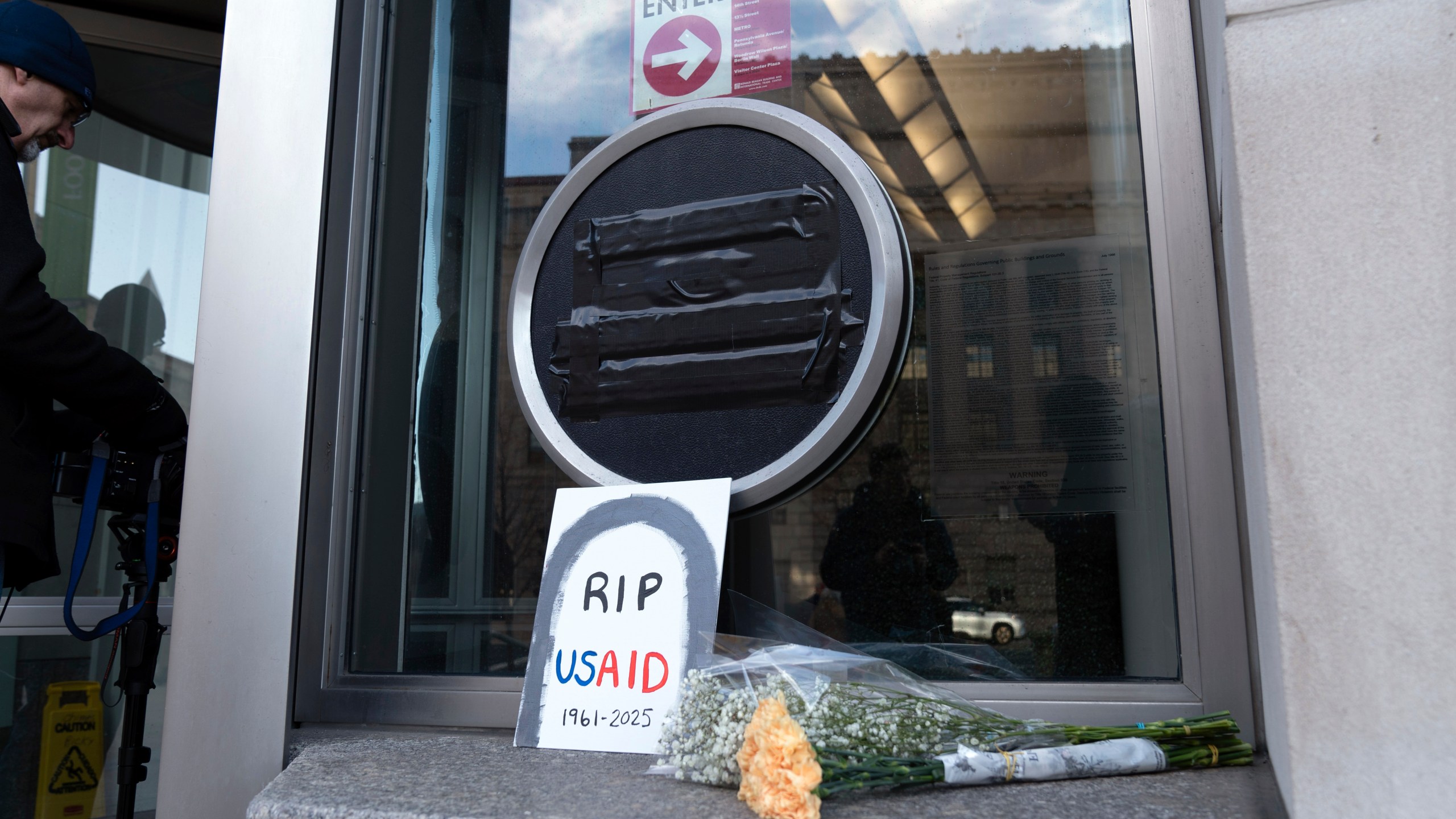 Flowers and a sign are placed outside the headquarters of the U.S. Agency for International Development, or USAID, Friday, Feb. 7, 2025, in Washington. (AP Photo/Jose Luis Magana)