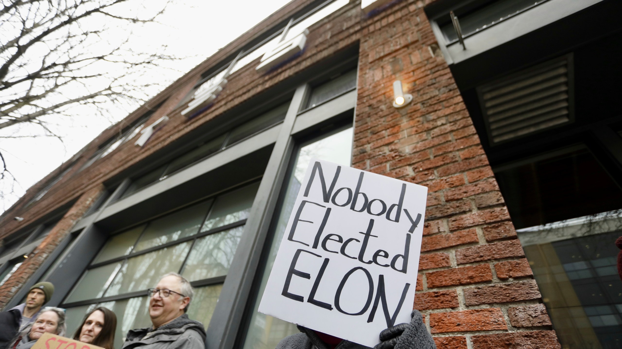 A person protesting Elon Musk's actions in the Trump administration holds a sign outside a Tesla showroom in Seattle on Thursday, Feb. 13, 2025. (AP Photo/Manuel Valdes)