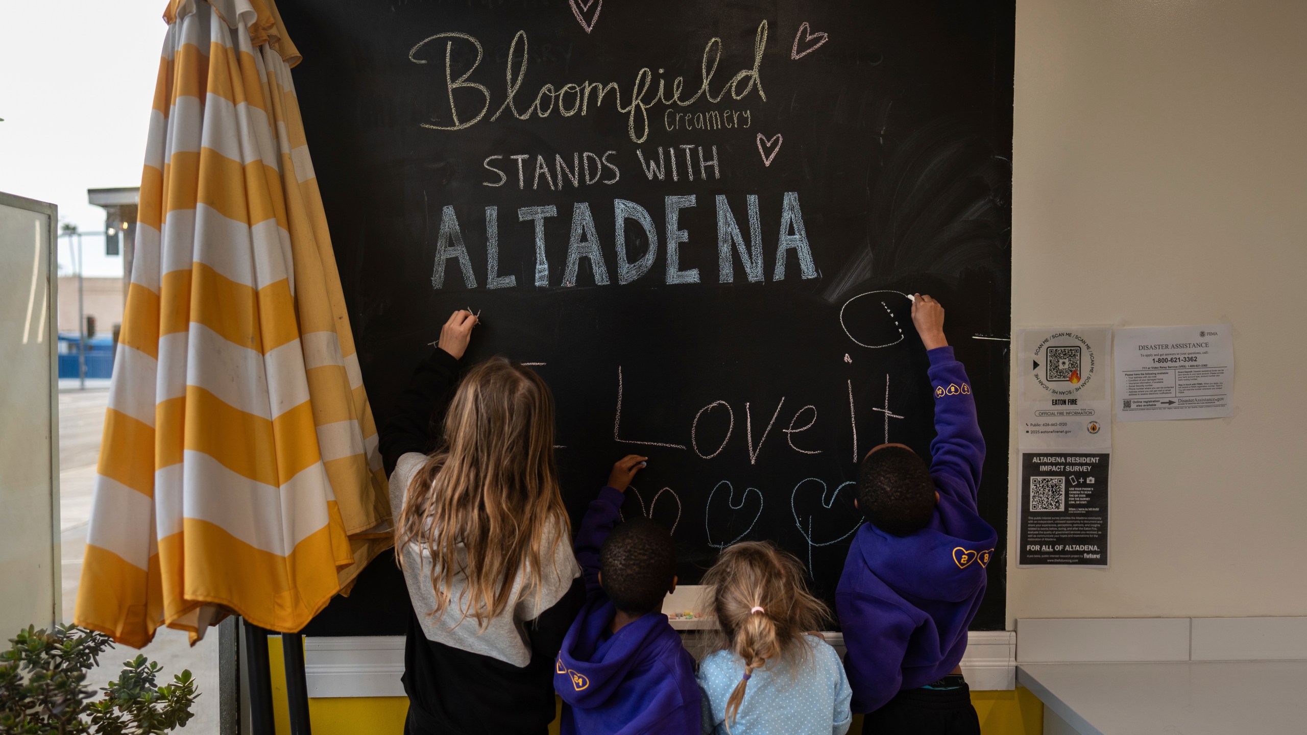 Eaton Fire evacuees Ceiba Phillips, from left, Russell Graham, Ceiba's sister, Quoia, and Russell's brother, Justin, draw on a blackboard at an ice cream shop in Pasadena, Calif., Wednesday, Feb. 5, 2025. (AP Photo/Jae C. Hong)