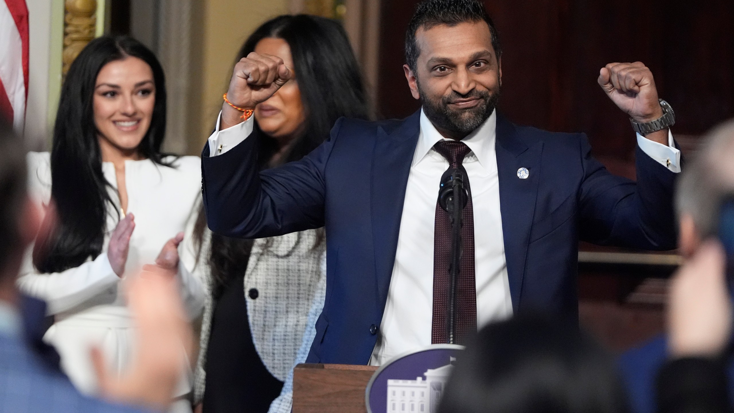 Kash Patel raises his fists in celebration during a news conference while Alexis Wilkins claps