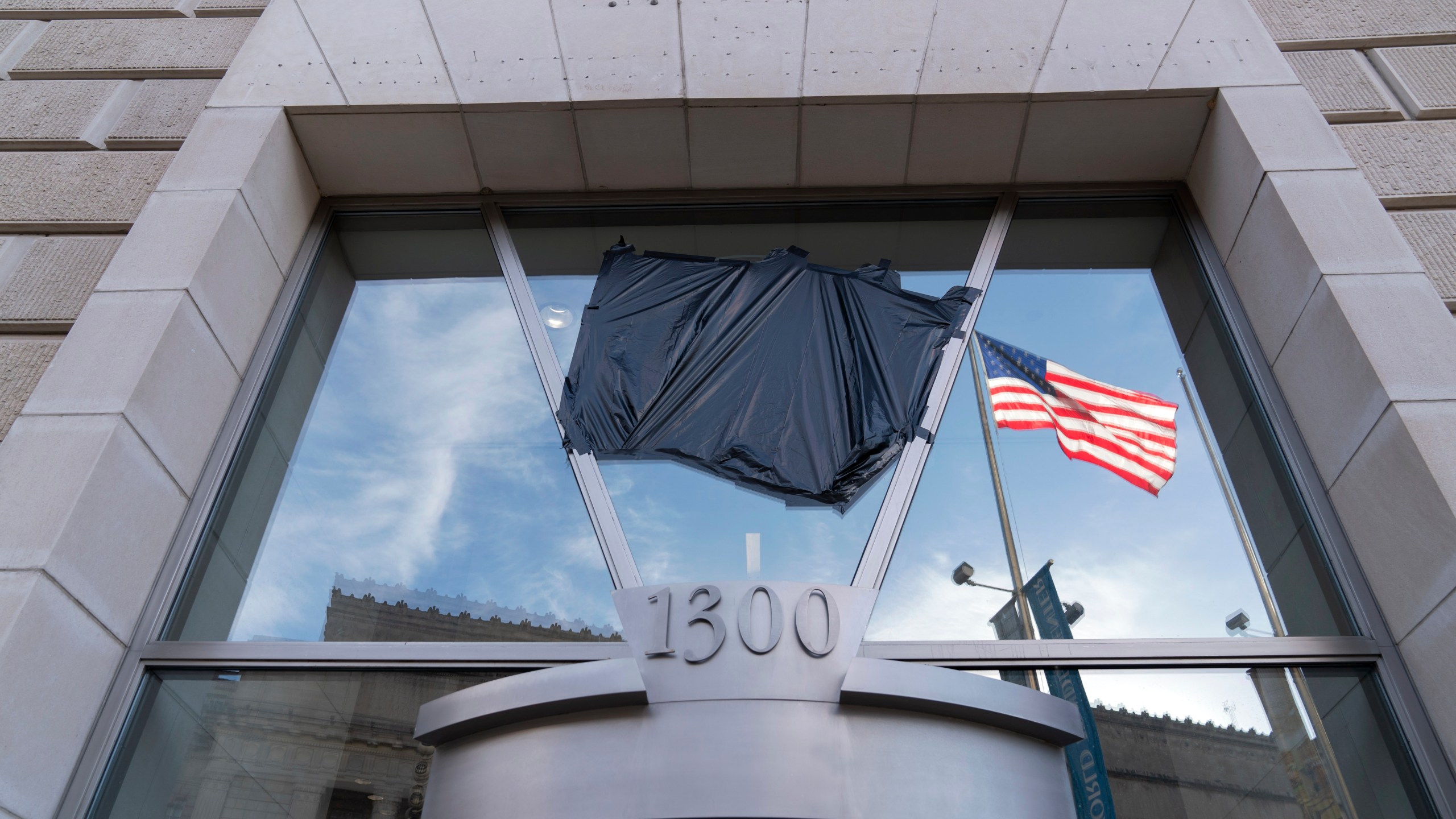 The American flag flying alone beside an empty flagpole that previously had the flag of the U.S. Agency for International Development, or USAID, are pictured in the reflection of a window that previously had the sign and the seal of USAID, outside the agency's headquarters in Washington, Friday, Feb. 7, 2025. (AP Photo/Jose Luis Magana)