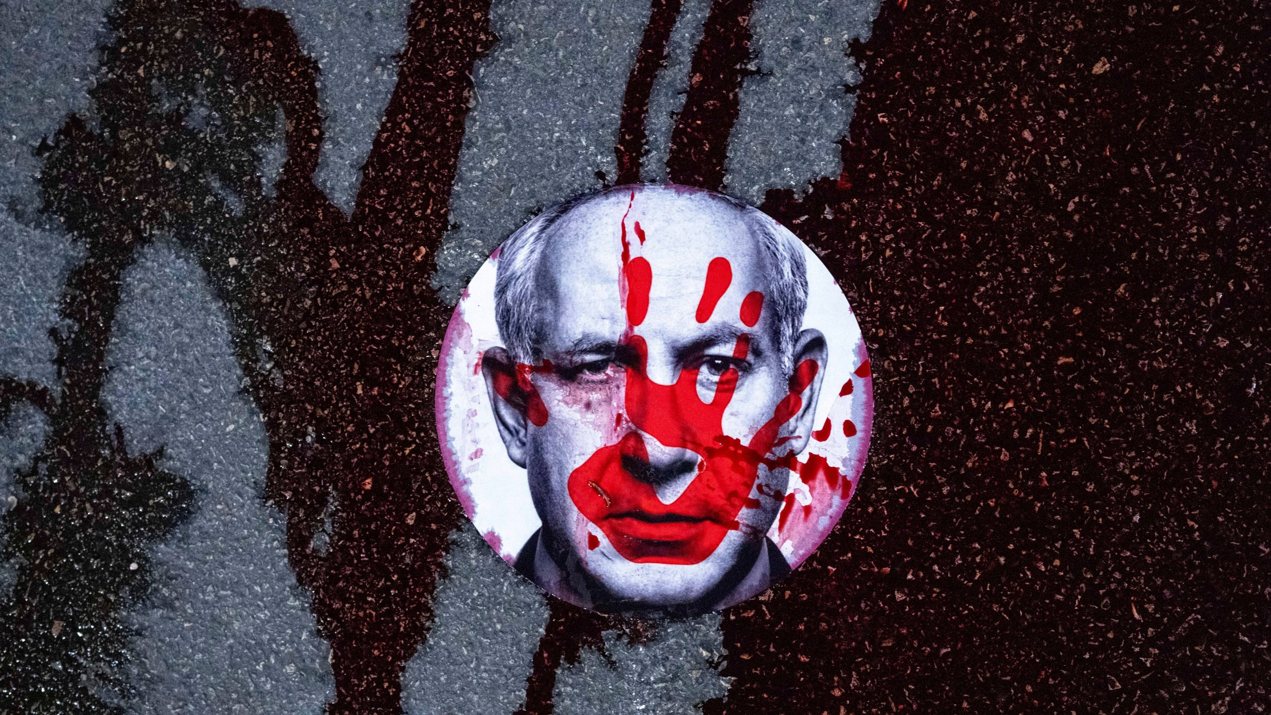 FILE - Supporters of Israelis held hostage by Hamas in Gaza stuck a sticker with the face of Israeli Prime Minister Benjamin Netanyahu on a road and poured red liquid, symbolizing blood, over it, in Jerusalem, Feb. 17, 2025. (AP Photo/Ohad Zwigenberg, File)