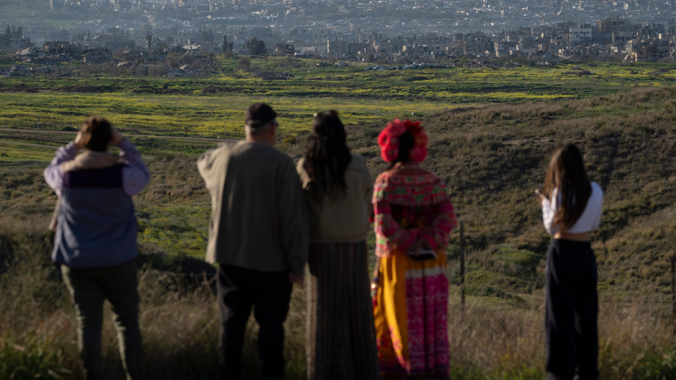 People look at buildings that were destroyed during the Israeli air and ground offensive stand in the Gaza Strip as seen from southern Israel, Sunday, March 2, 2025. (AP Photo/Leo Correa)