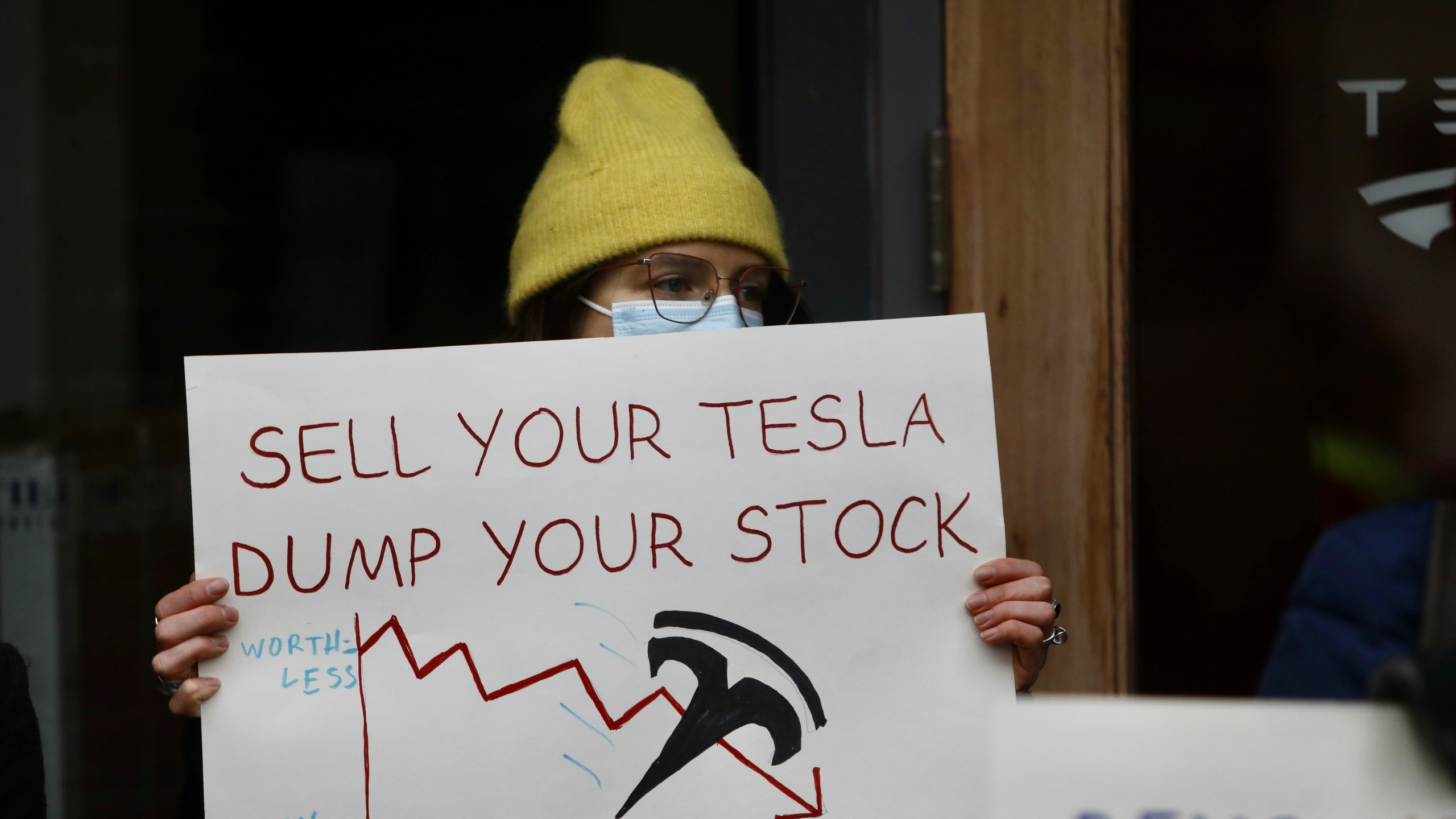 FILE - A person protesting Elon Musk's actions in the Trump administration holds a sign outside a Tesla showroom in Seattle, Thursday, Feb. 13, 2025. (AP Photo/Manuel Valdes, File)