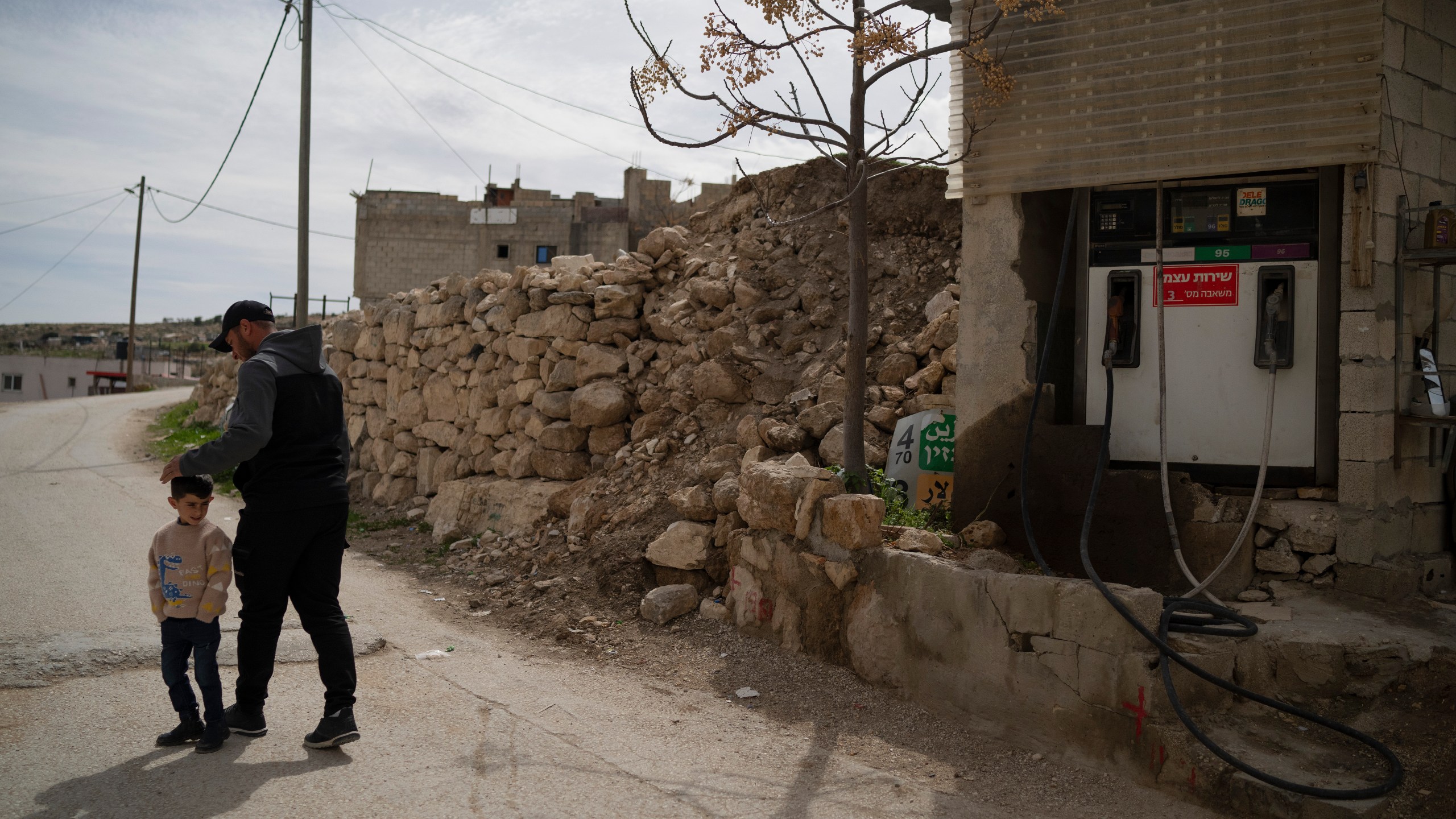 Salem Adra, walks with his 4-year-old son Elias, past his family's gas station, featured in the Oscar-winning documentary "No Other Land," co-directed by his brother Palestinian activist Basel Adra, at the West Bank village of Tuwani, Monday, March 3, 2025. (AP Photo/Leo Correa)