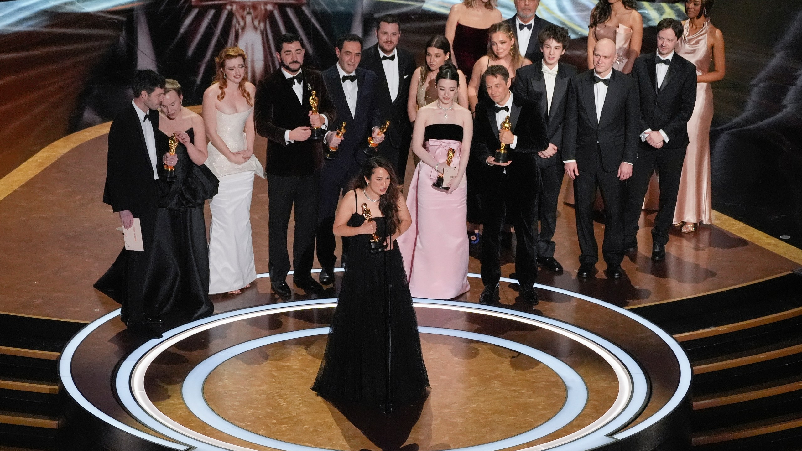 Samantha Quan, front center, accepts the award for best picture for "Anora" during the Oscars on Sunday, March 2, 2025, at the Dolby Theatre in Los Angeles. Alex Coco, from rear left, Darya Ekamasova, Lindsey Normington, Vache Tovmasyan, Karren Karagulian, Vincent Radwinsky, Luna Sofía Miranda, Mikey Madison, Sean Baker, Mark Eydelshteyn, Yura Borisov, Meg Ryan, and Billy Crystal look on from back. (AP Photo/Chris Pizzello)