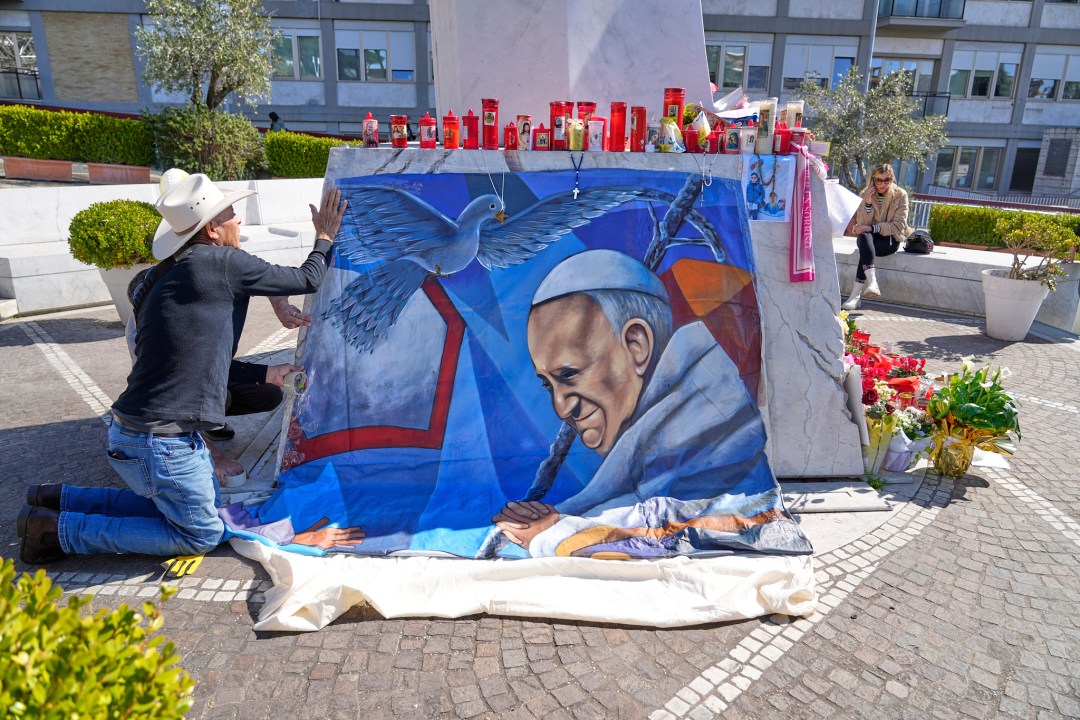 An artist places a painting of Pope Francis outside a hospital