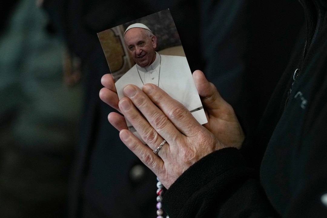 A woman's hands are clasped in prayer around a photo of Pope Francis